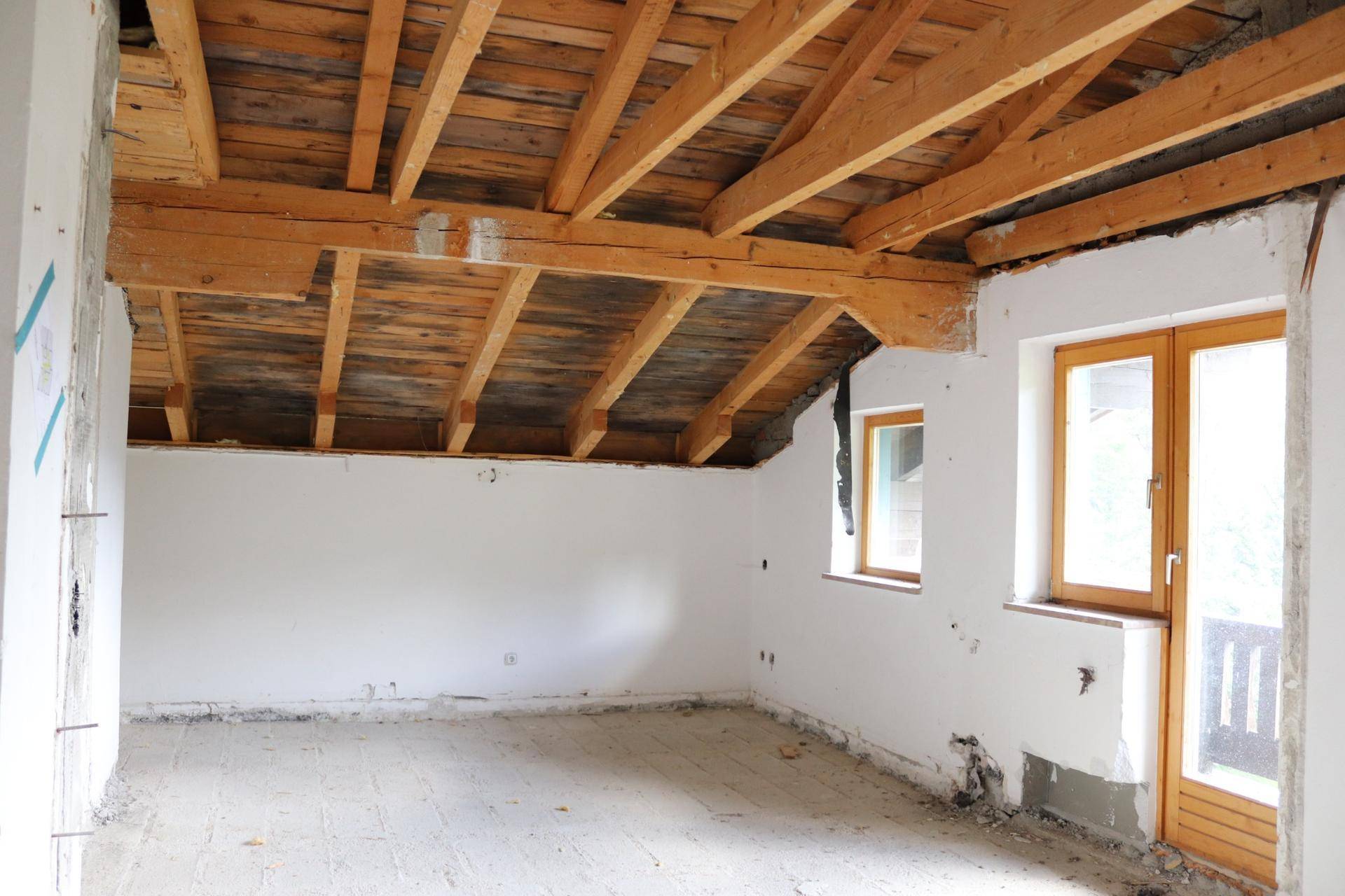 Dachgeschossraum im Rohbau mit sichtbaren Holzbalken und Fenstern, bereit für den Ausbau.