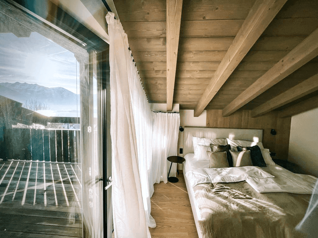 Helles Schlafzimmer mit Holzbalkendecke und direktem Zugang zu einem Balkon mit Bergblick.