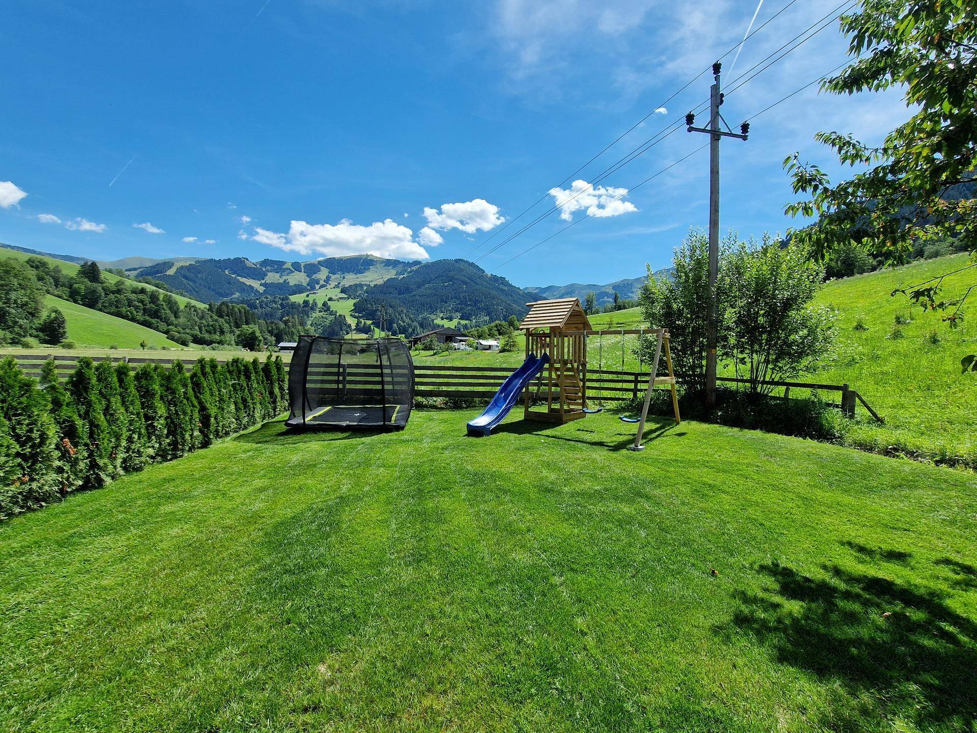 Großer grüner Garten mit Spielplatz, Trampolin und Blick auf die umliegende Berglandschaft.