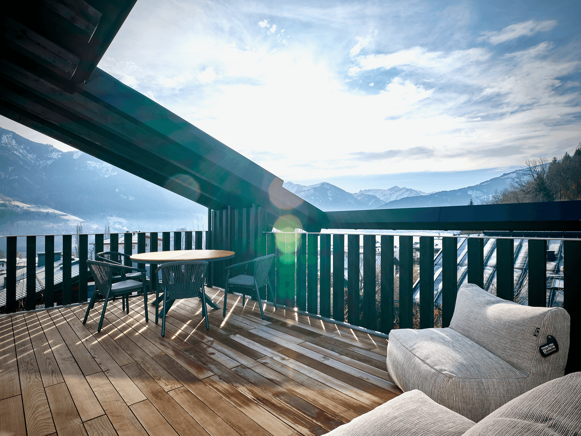 Sonniger Balkon mit bequemen Sitzgelegenheiten und spektakulärem Blick auf die umliegende Berglandschaft und den See.