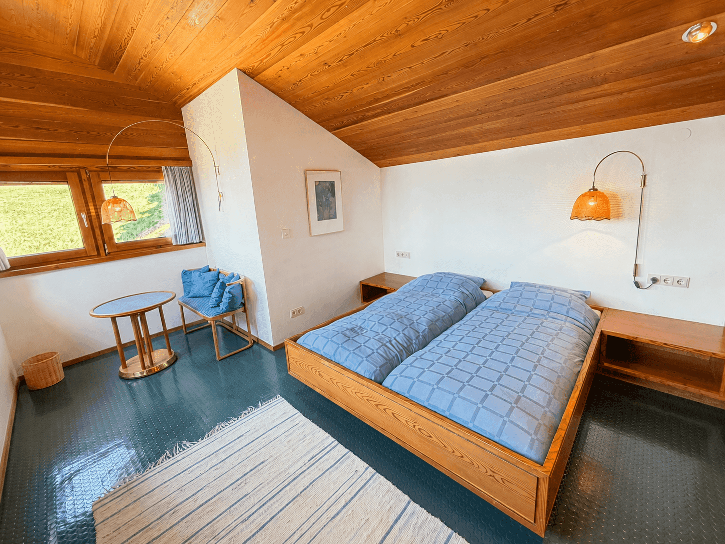 Schlafzimmer im Dachgeschoss mit Holzdachschräge, Doppelbett und Blick auf die Landschaft.