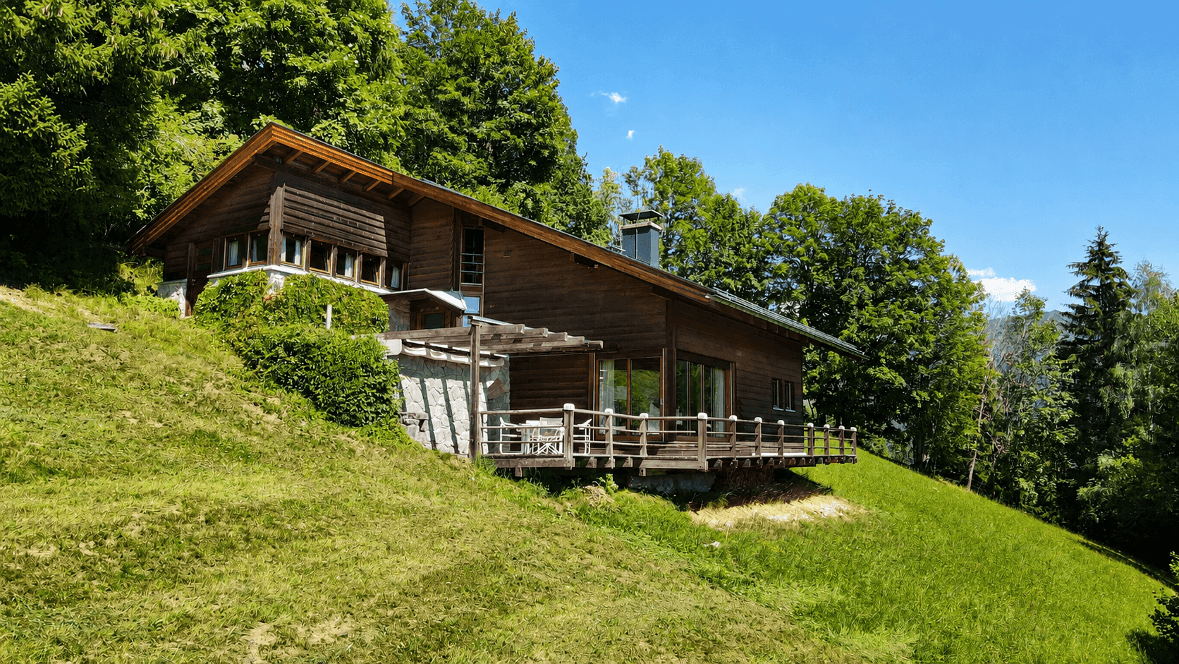 Charmantes Holzhaus mit Terrasse, umgeben von üppigem Grün und Bäumen in den Bergen.