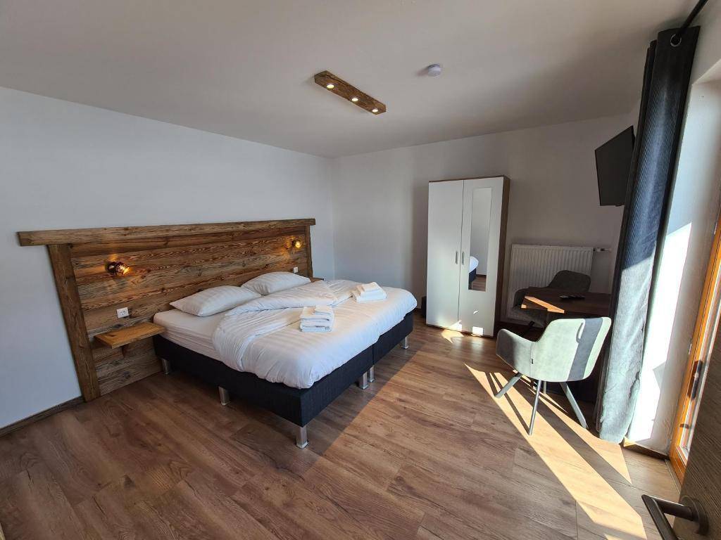 Helles Schlafzimmer mit Holzboden, Doppelbett, weißem Kleiderschrank und Schreibtischbereich.