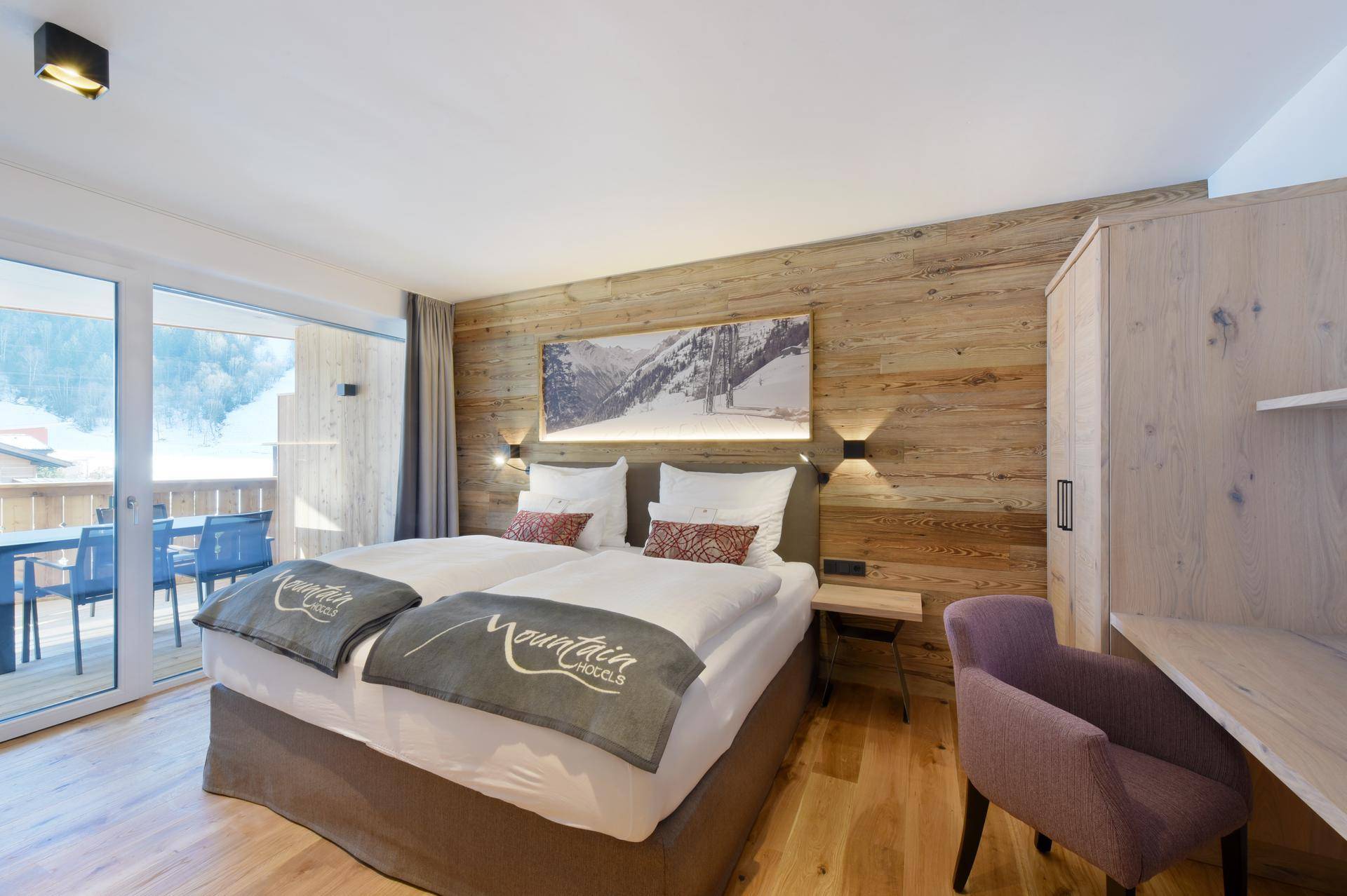Gemütliches Schlafzimmer mit Holzwand, Doppelbett und Zugang zu einem möblierten Balkon.