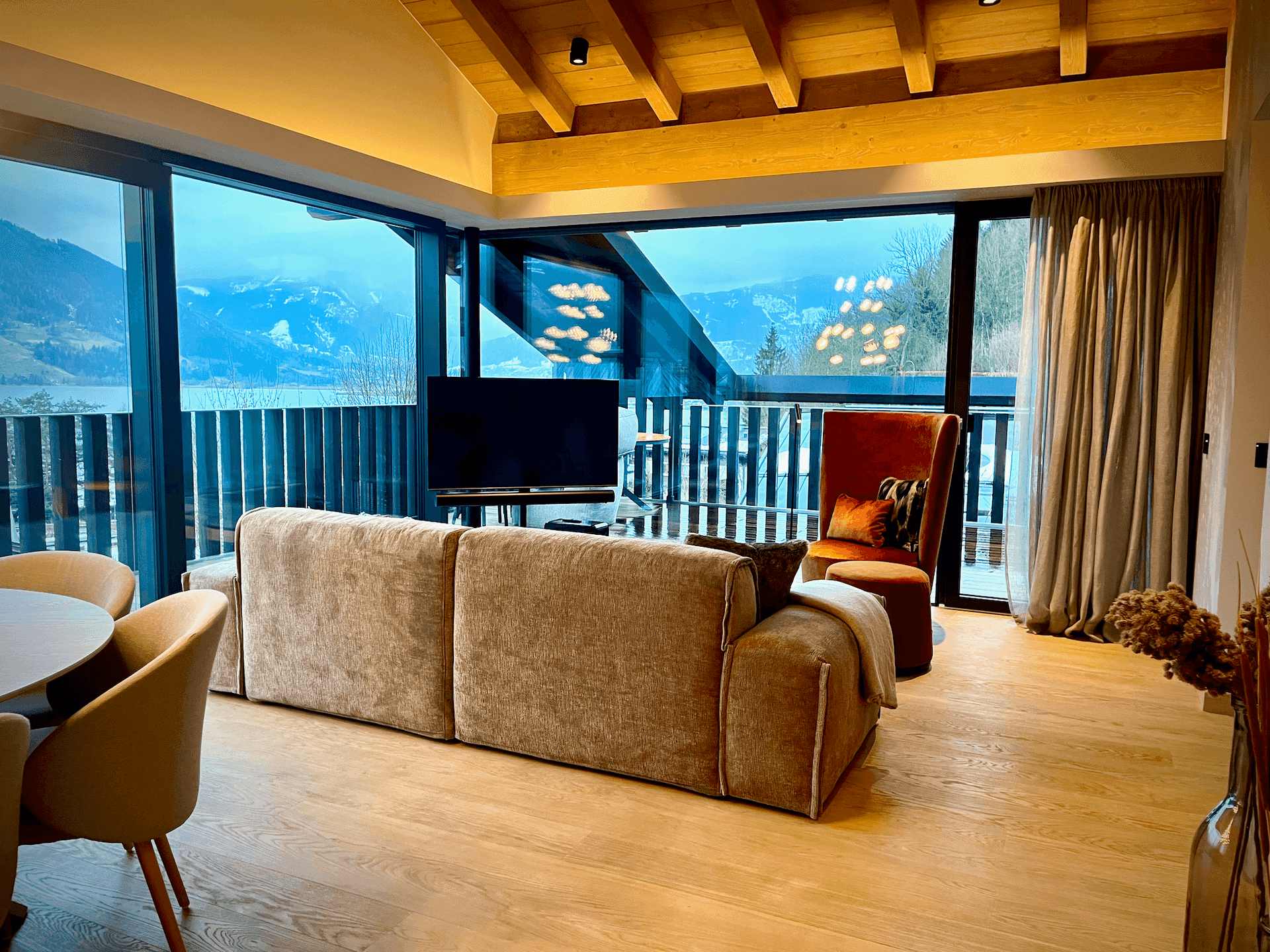 Geräumiger Wohnbereich mit bequemer Couch, Esstisch und großen Fenstern mit See- und Bergblick.