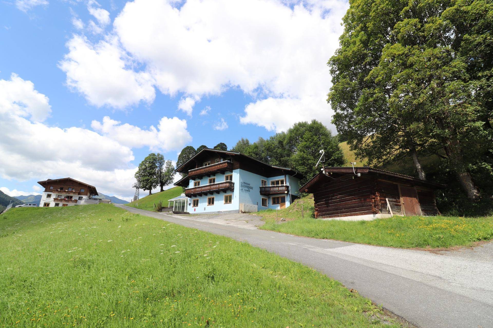 Weitläufige Ansicht des Hauses in ländlicher Umgebung mit weiteren Gebäuden und einem Holzschuppen.