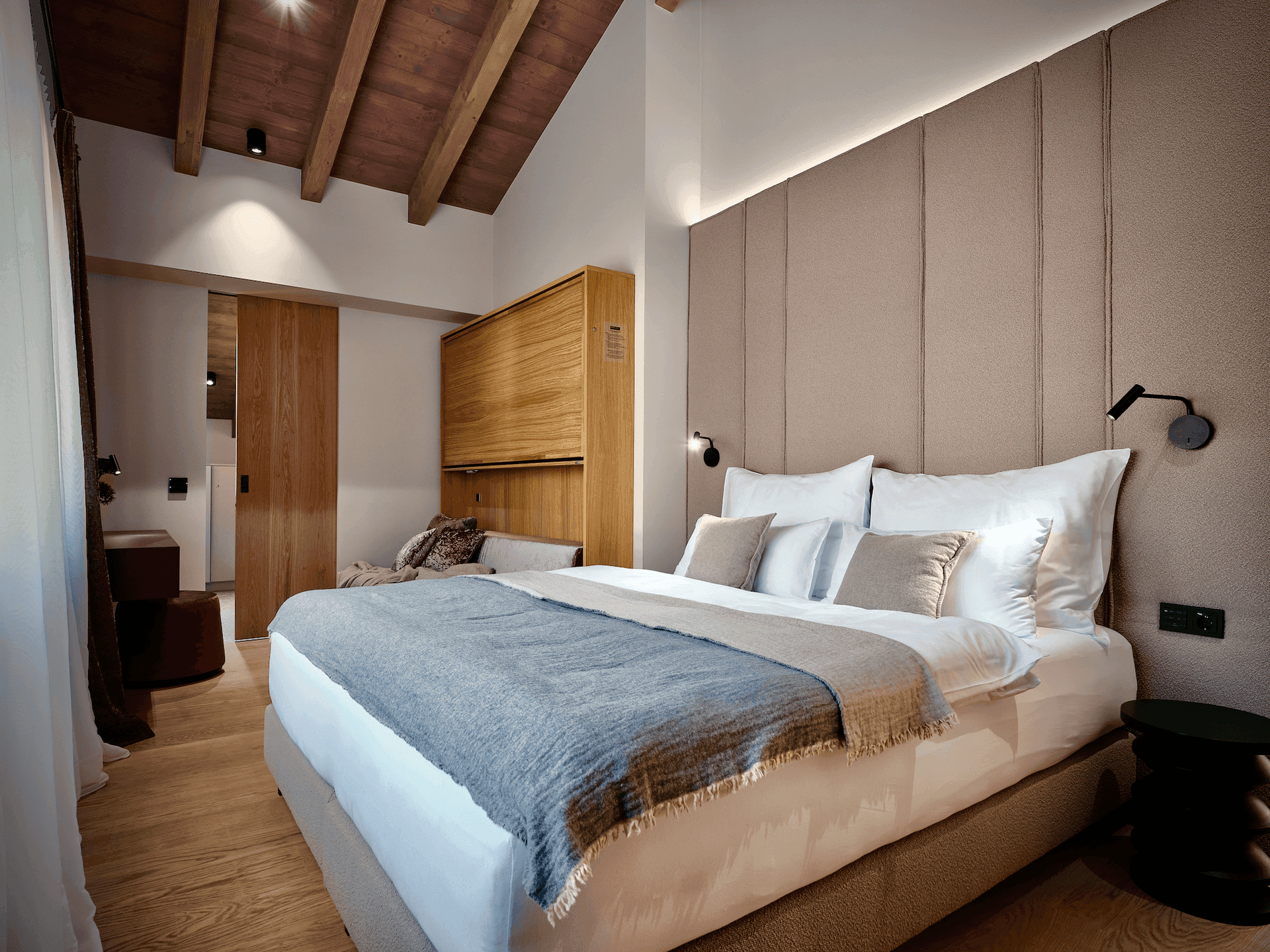 Schlafzimmer mit großem Bett, gepolstertem Kopfteil und sichtbaren Holzbalken an der Decke.