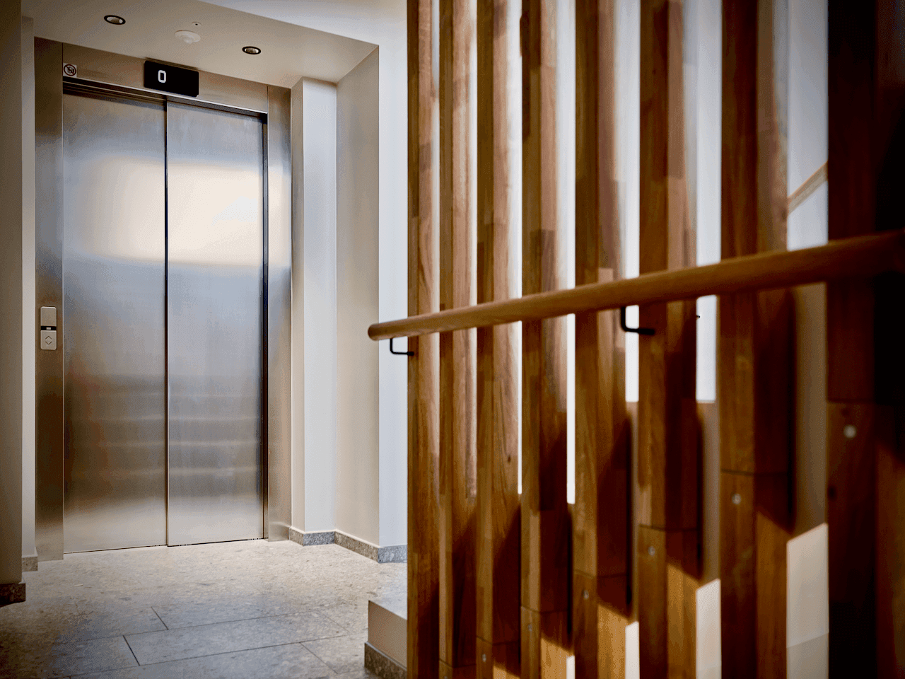 Moderner Eingangsbereich mit Edelstahllift und dekorativer Holzlamellenwand neben der Treppe.