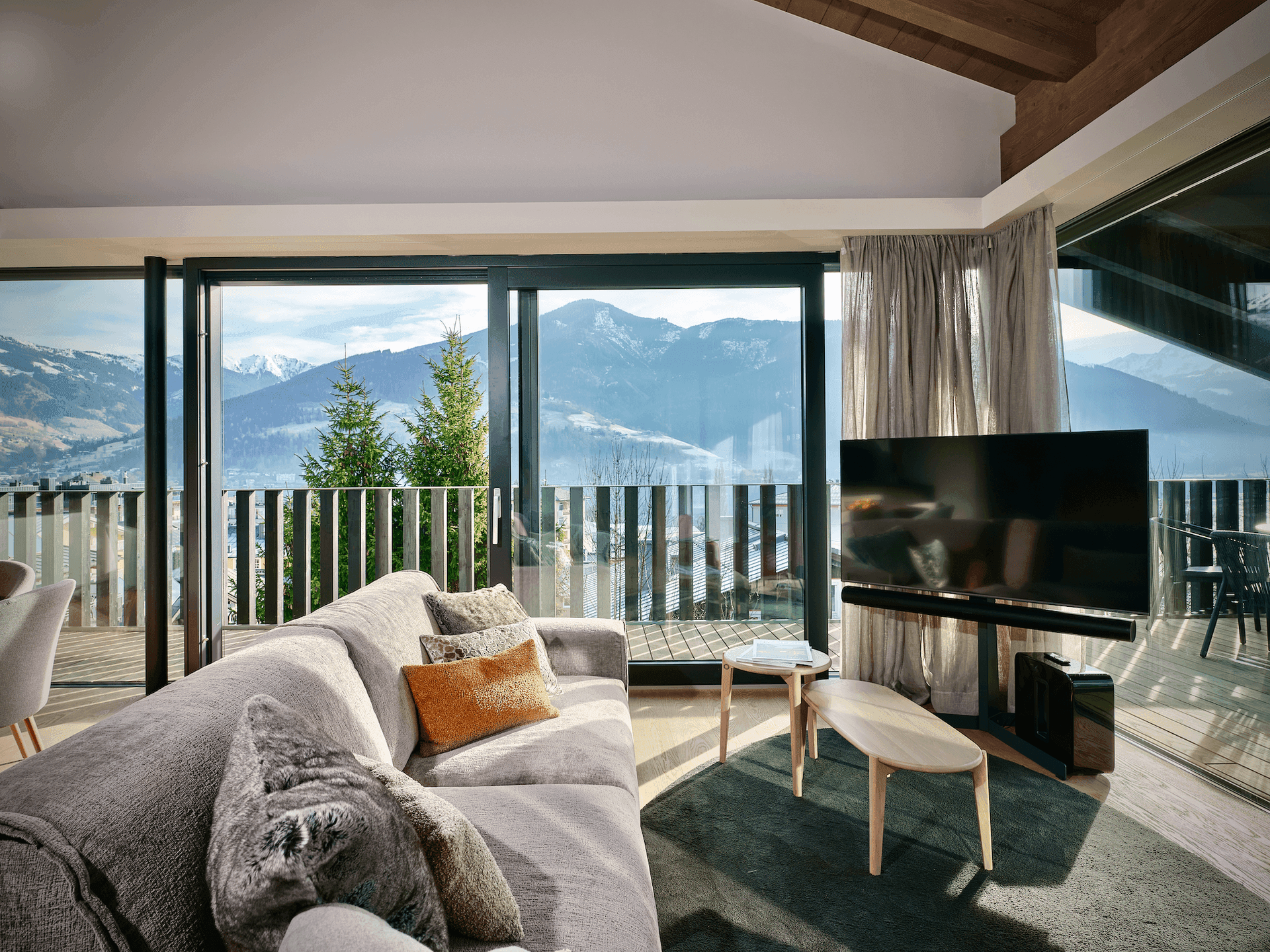 Gemütliches Wohnzimmer mit großem Sofa und Panoramafenstern, die einen weiten Bergblick bieten.
