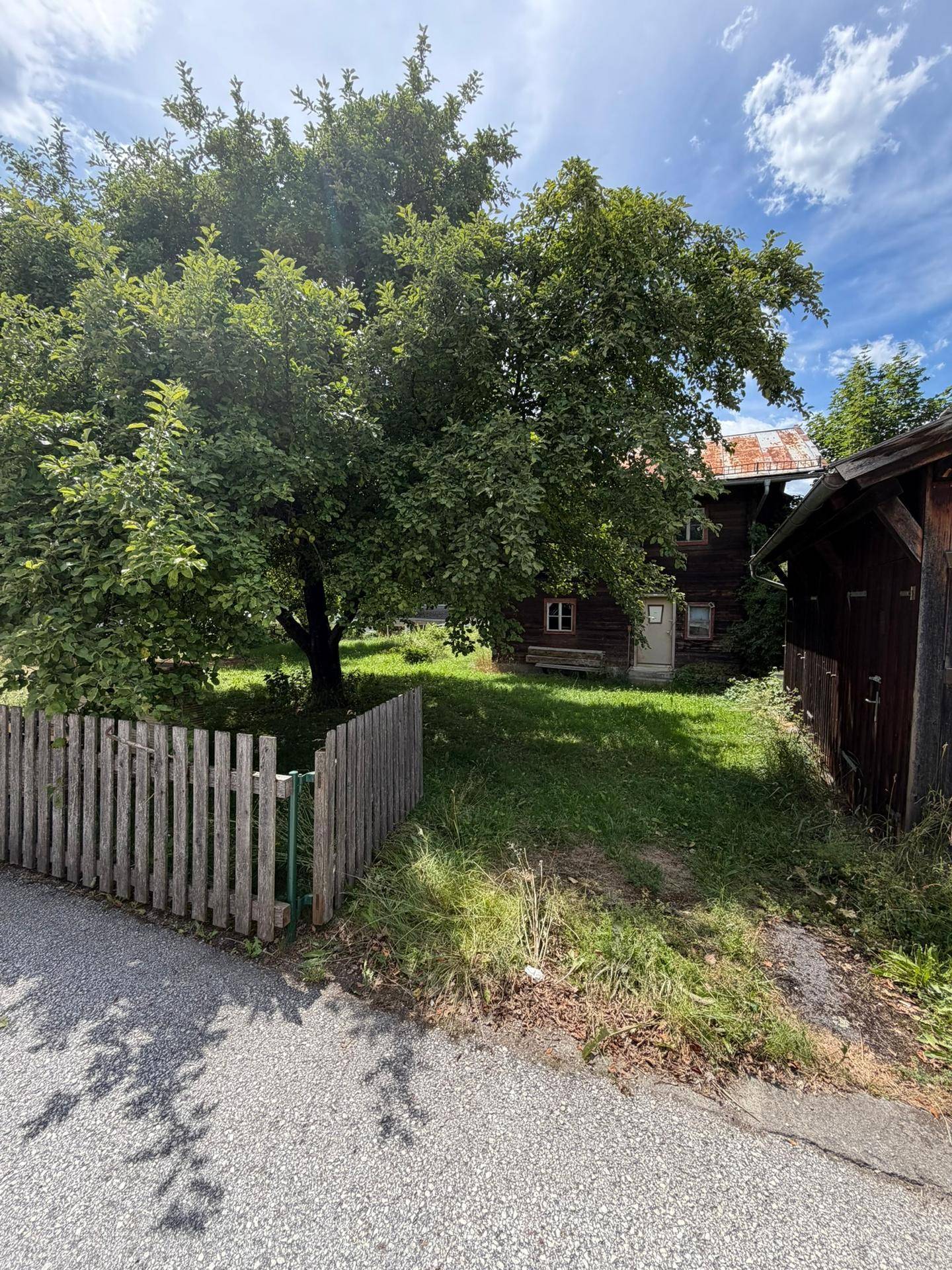 Idyllischer Gartenbereich mit Holzzaun, großem Baum und einem charmanten Holzhaus im ländlichen Stil.