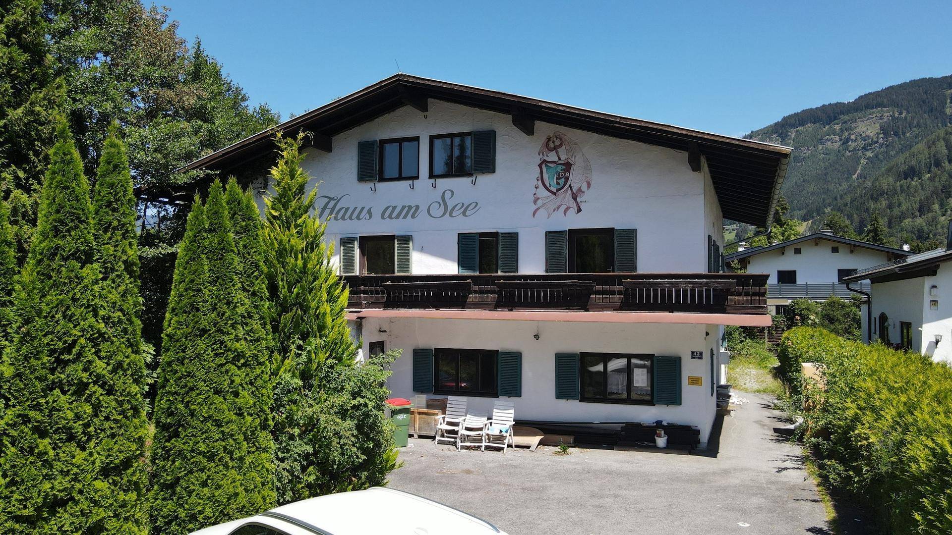 Gesamtansicht des traditionellen Gebäudes mit Balkonen, umgeben von Bäumen und Bergen.