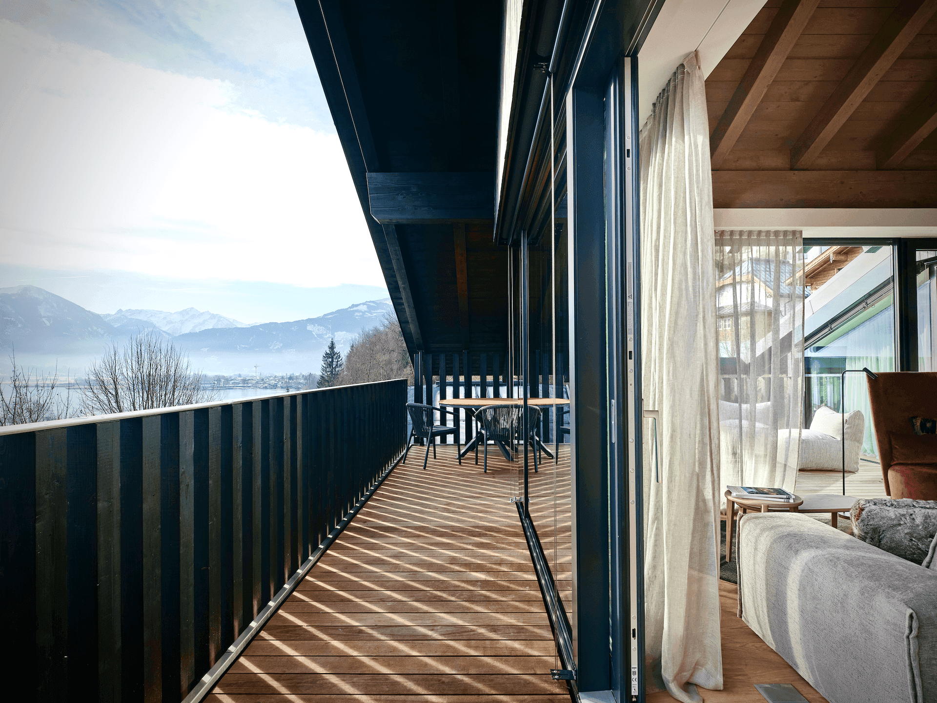Geräumiger Balkon mit Holzboden und Sitzgelegenheiten, bietet einen weiten Blick auf See und Berge.