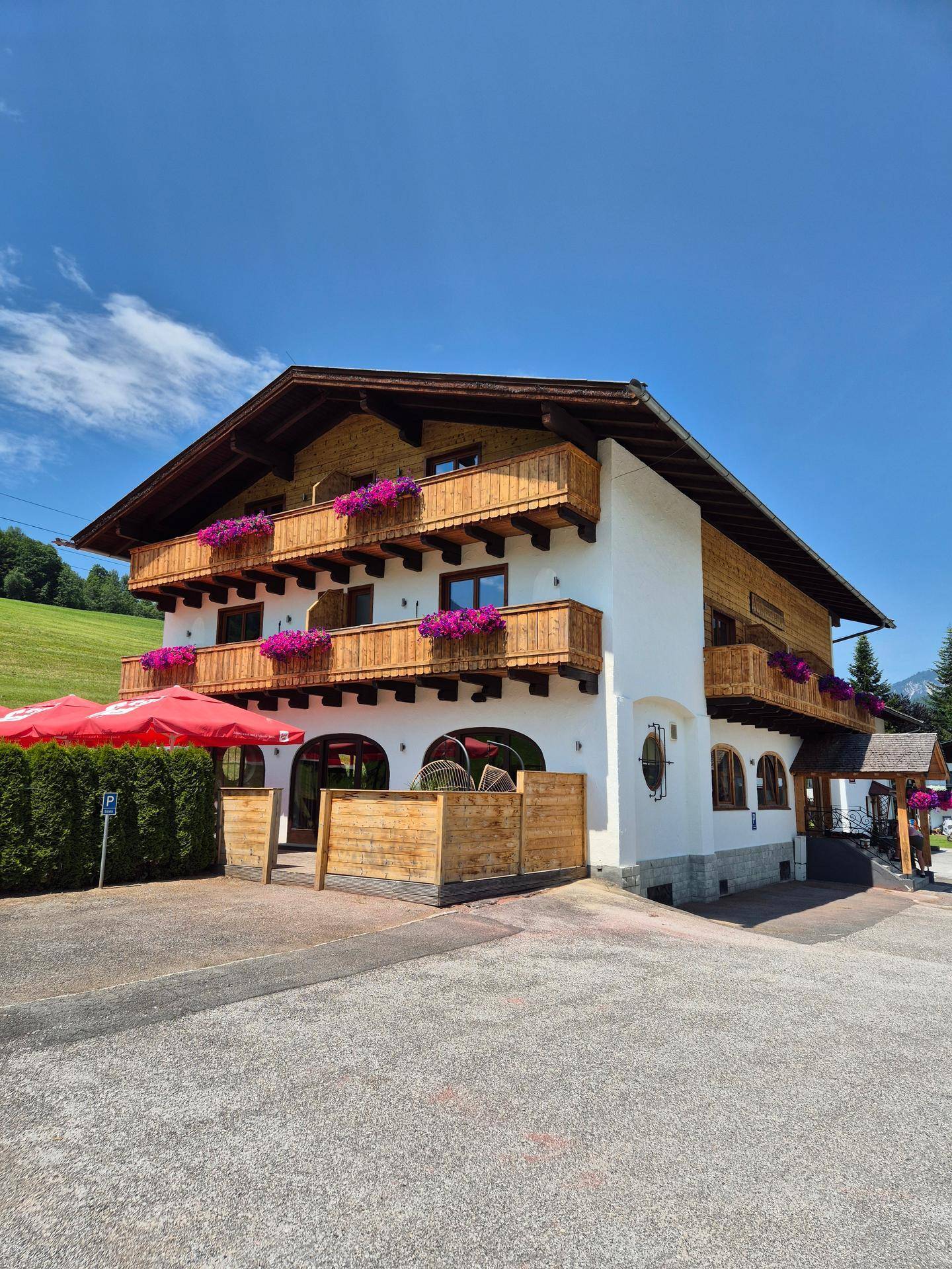 Traditionelles Gebäude mit Holzbalkonen, Blumenkästen und einem Parkplatz im Freien.