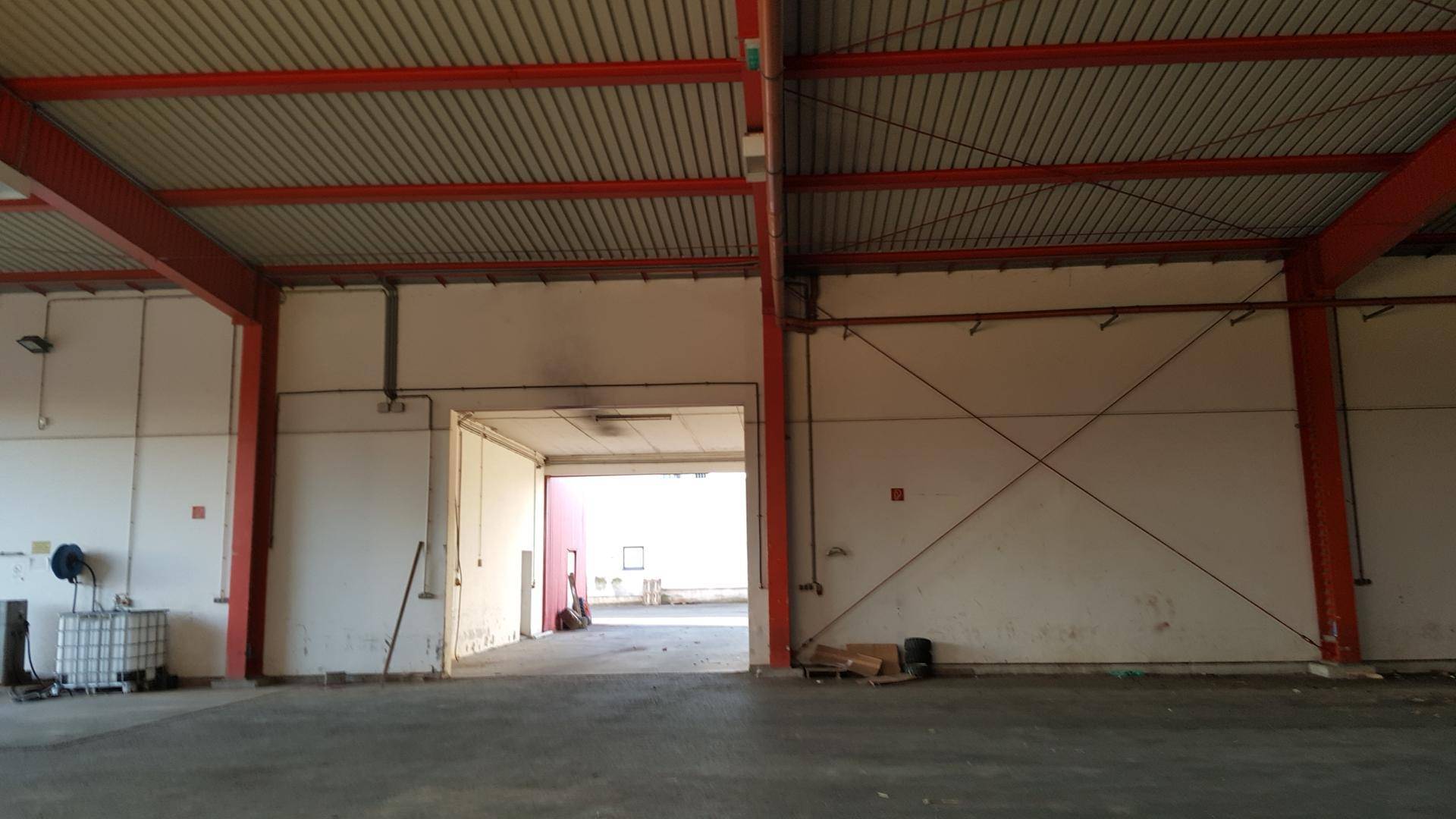 Weitläufige Lagerhalle mit roter Stahlkonstruktion und offenem Durchgang zu einem weiteren Bereich.