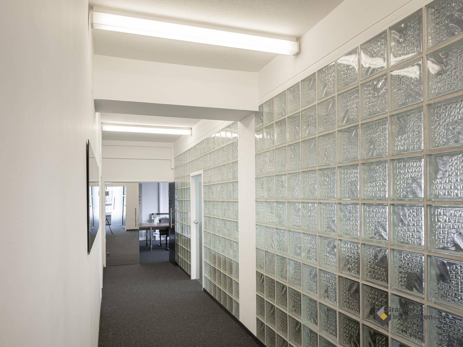 Heller Bürogang mit einer markanten Glasbausteinwand und grauem Teppichboden.