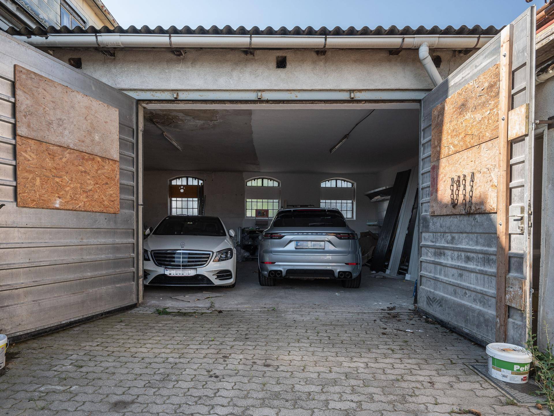 Geräumige Garage mit zwei Luxusautos, großen Holztoren und gepflastertem Boden.