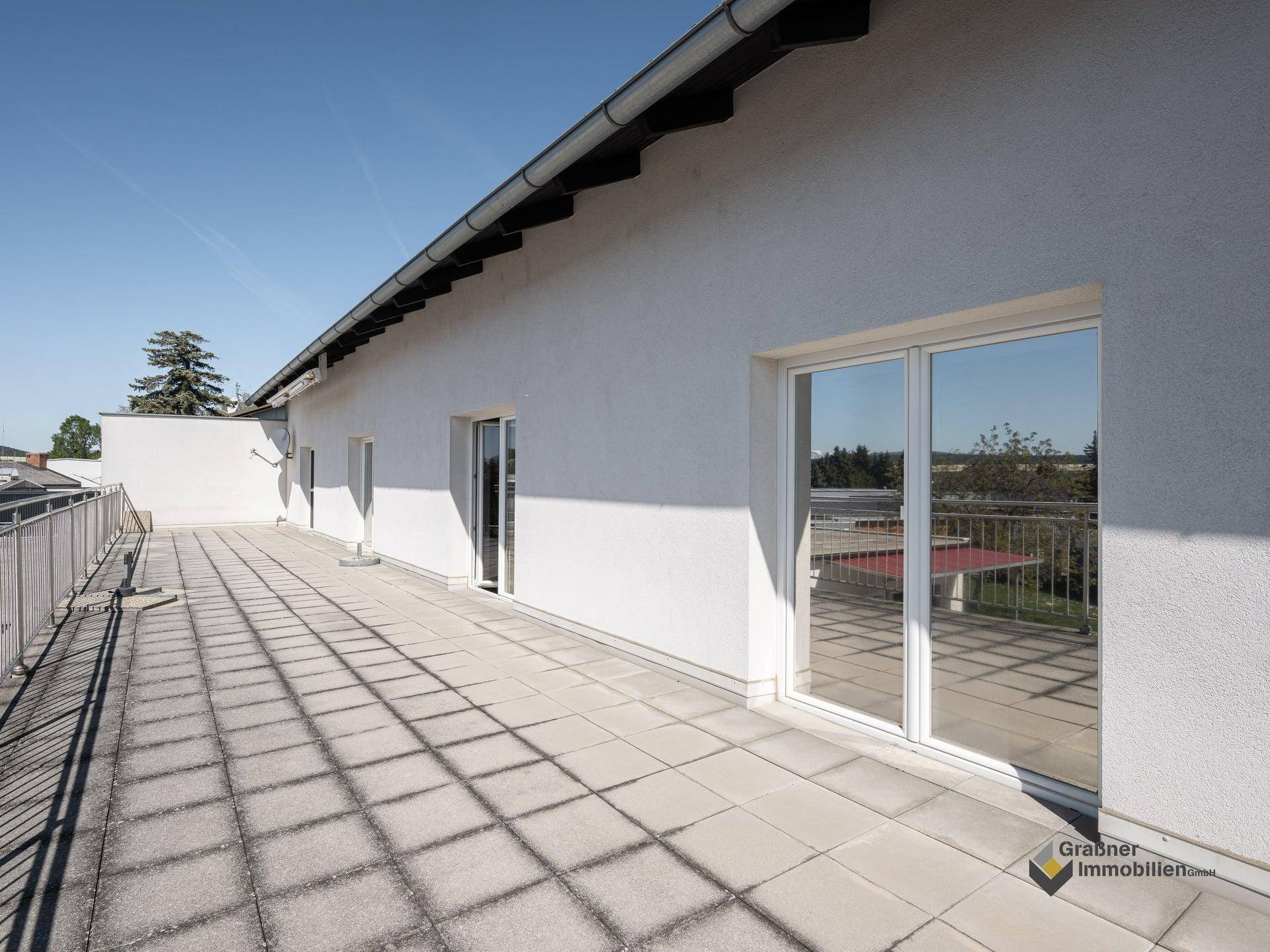 Große Dachterrasse mit Fliesenboden, Geländer und weitem Blick in die Landschaft.