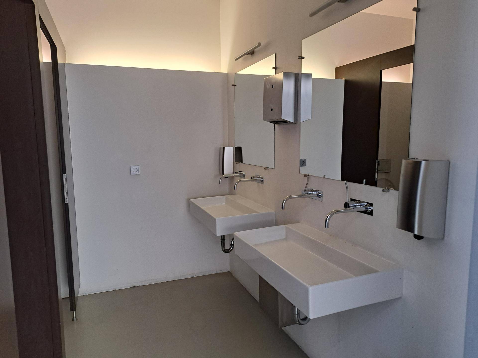 Modernes Badezimmer mit zwei wandmontierten Waschbecken, großen Spiegeln und Handtrocknern.