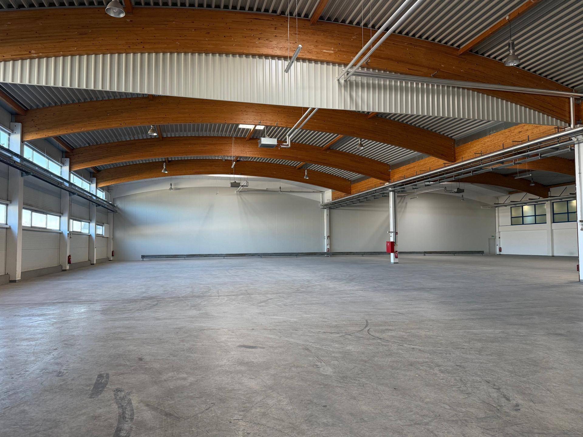 Helle und geräumige Lagerhalle mit hohen Decken, Holzträgern und Betonboden, bereit zur Nutzung.