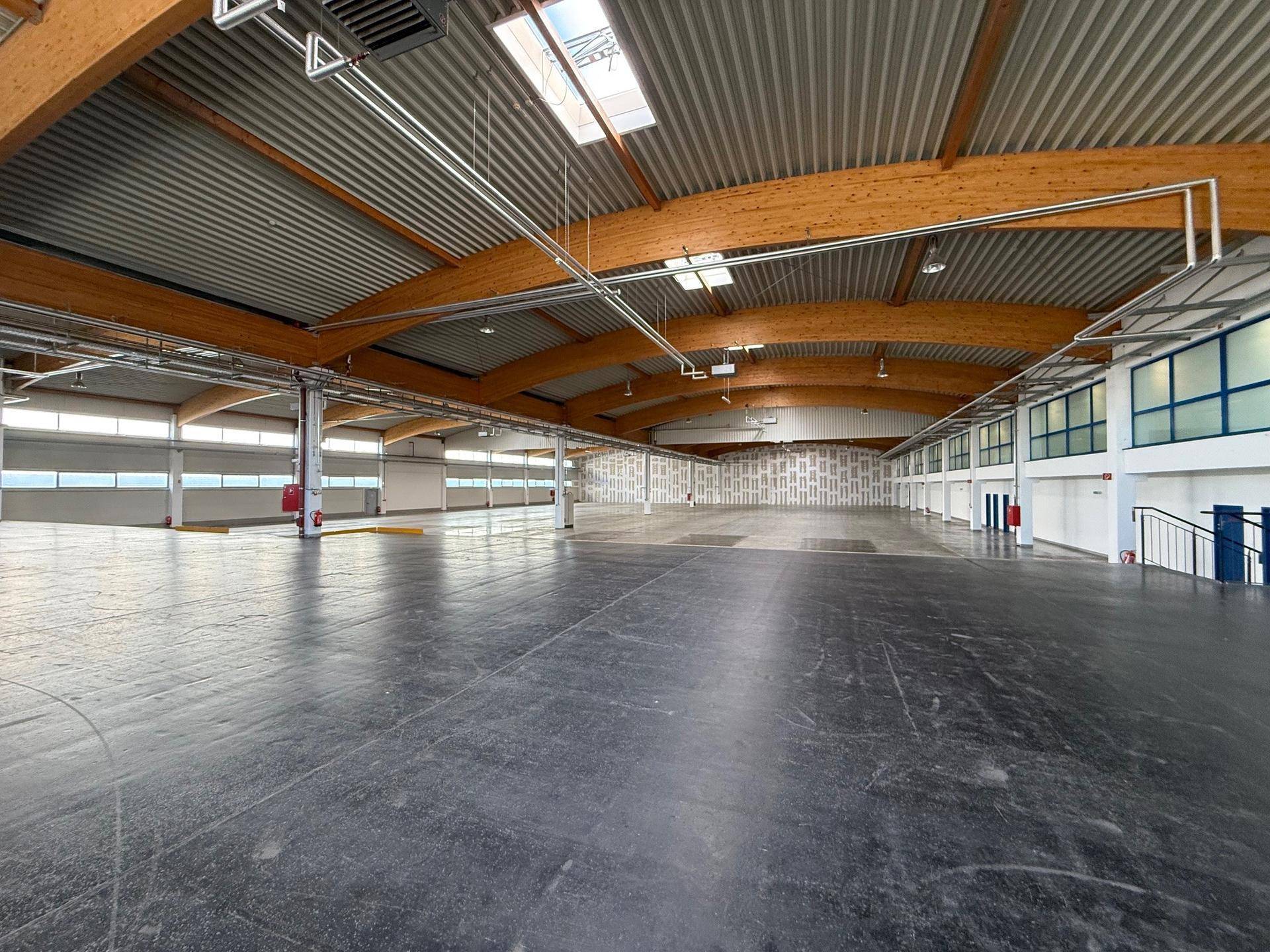 Weitläufige Lagerhalle mit hohen Decken, Holzträgern und Oberlichtern, bietet viel Platz und natürliches Licht.