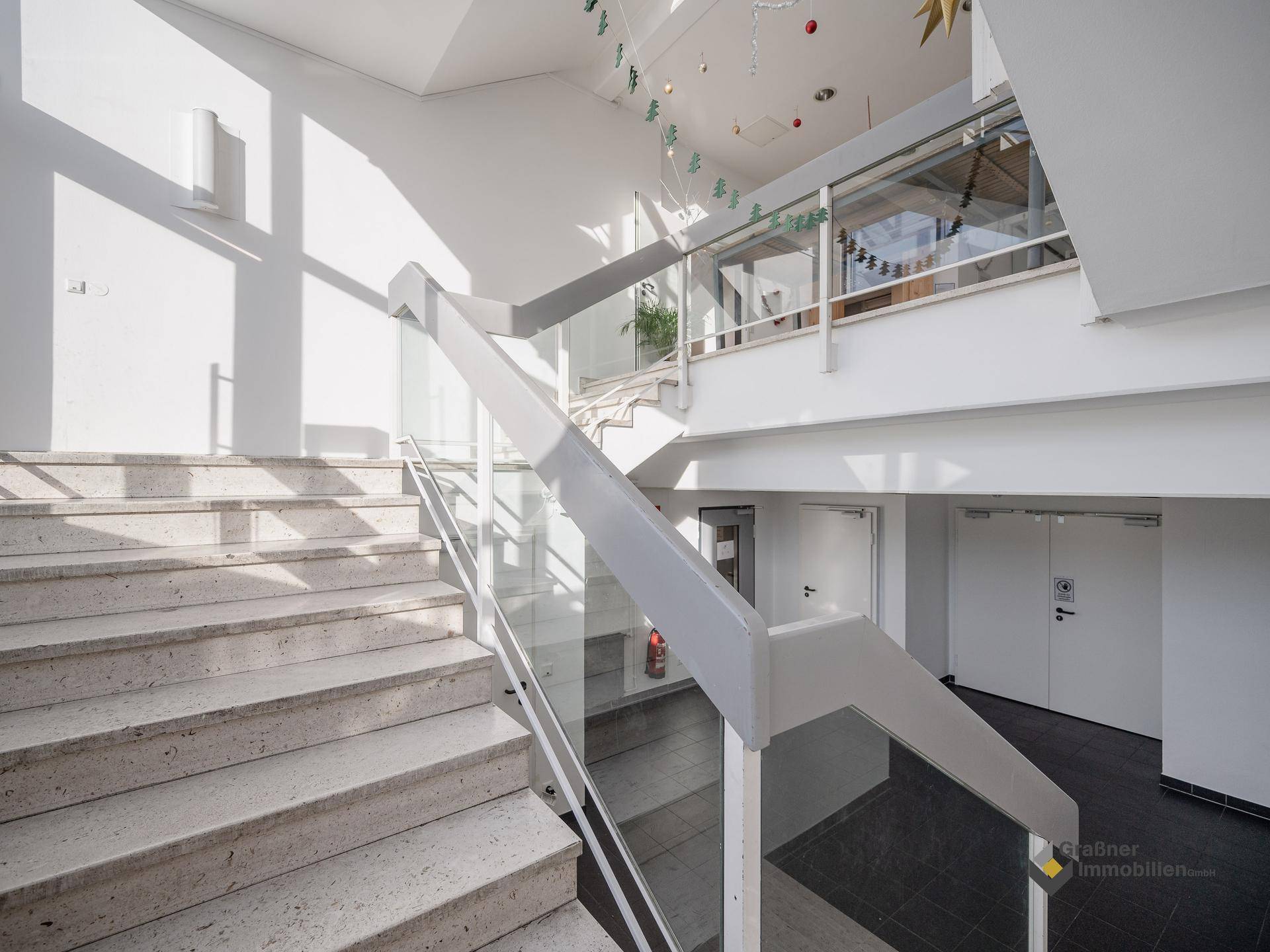 Helles, modernes Treppenhaus mit Steinstufen, Glasgeländer und festlicher Dekoration.