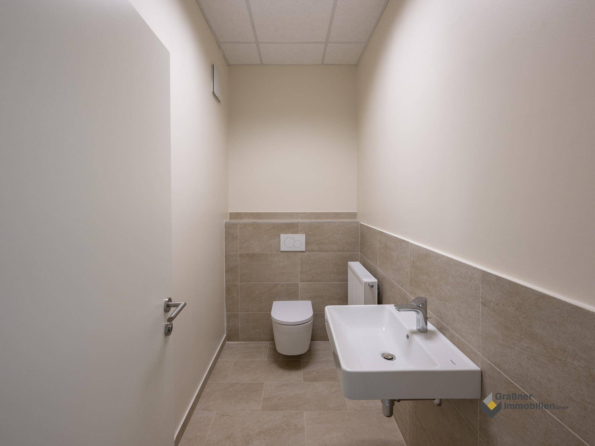 Modernes WC mit wandhängender Toilette und Waschbecken, halbhoch gefliest.