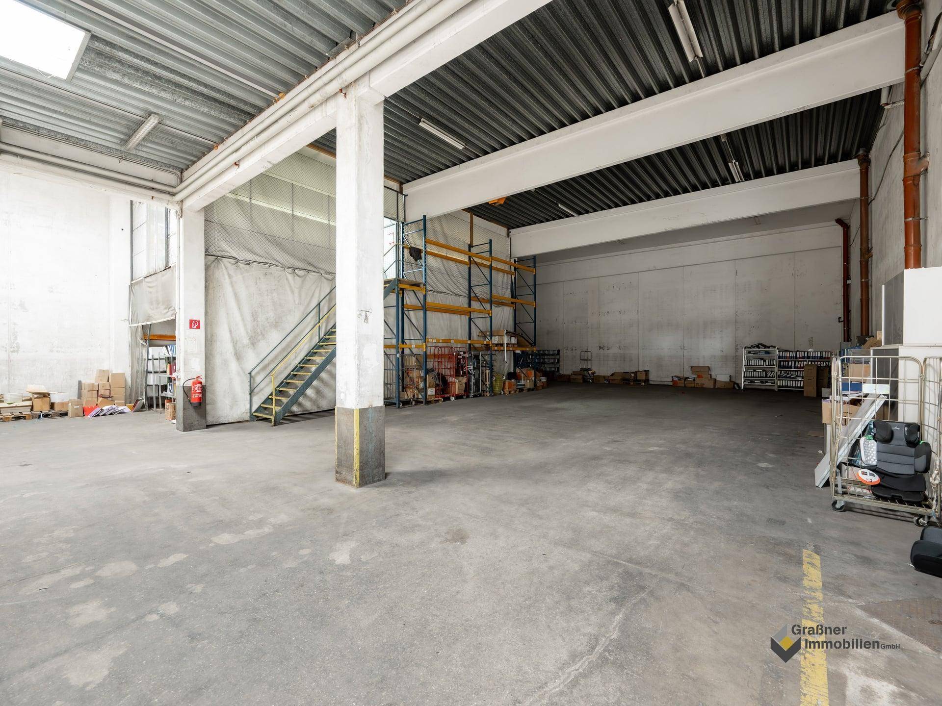 Weitläufige Lagerhalle mit Betonboden, hohen Decken und Regalsystemen an den Wänden.