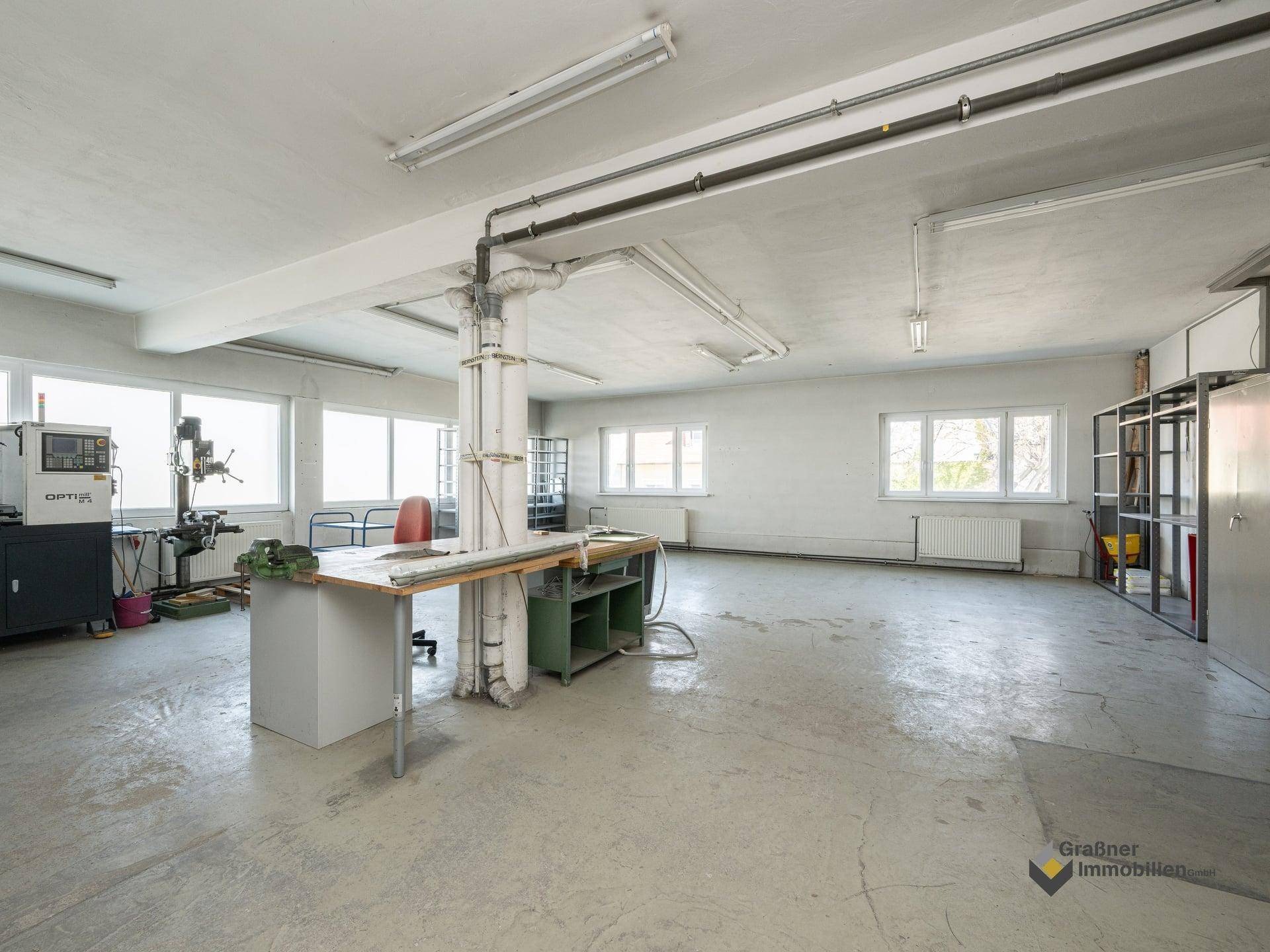 Großer Werkstattraum mit Betonboden, vielen Fenstern und industrieller Ausstattung.