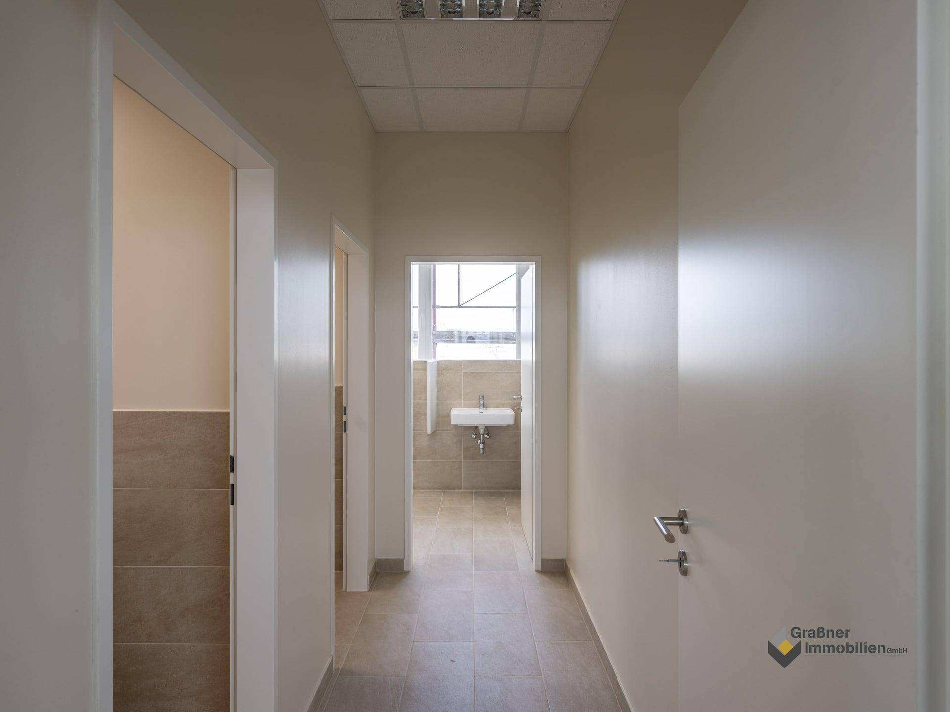 Heller Flur mit Fliesenboden, der zu einem Badezimmer oder einer Toilette führt.