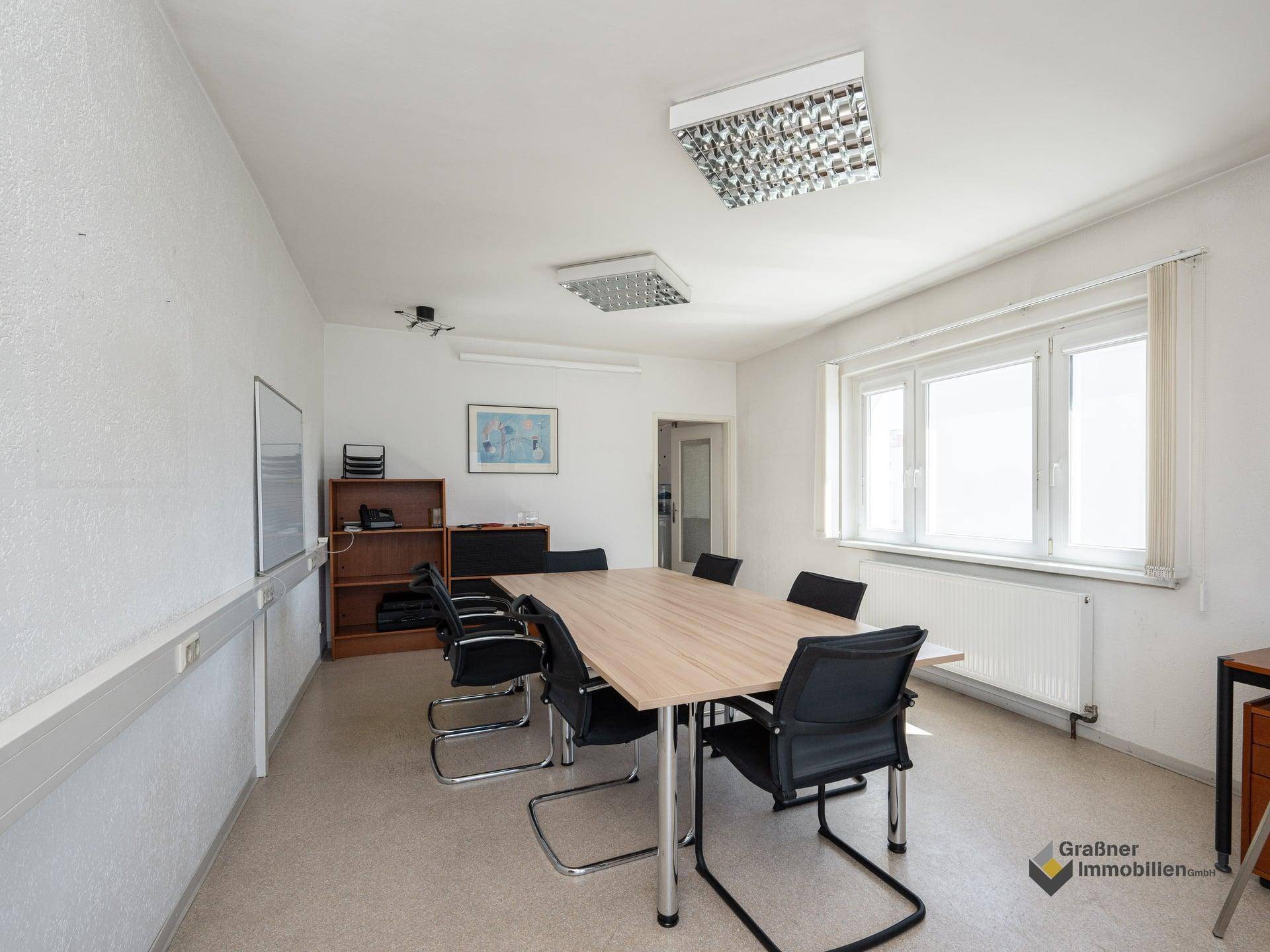 Heller Konferenzraum mit großem Holztisch, Bürostühlen und Fenster für Tageslicht.