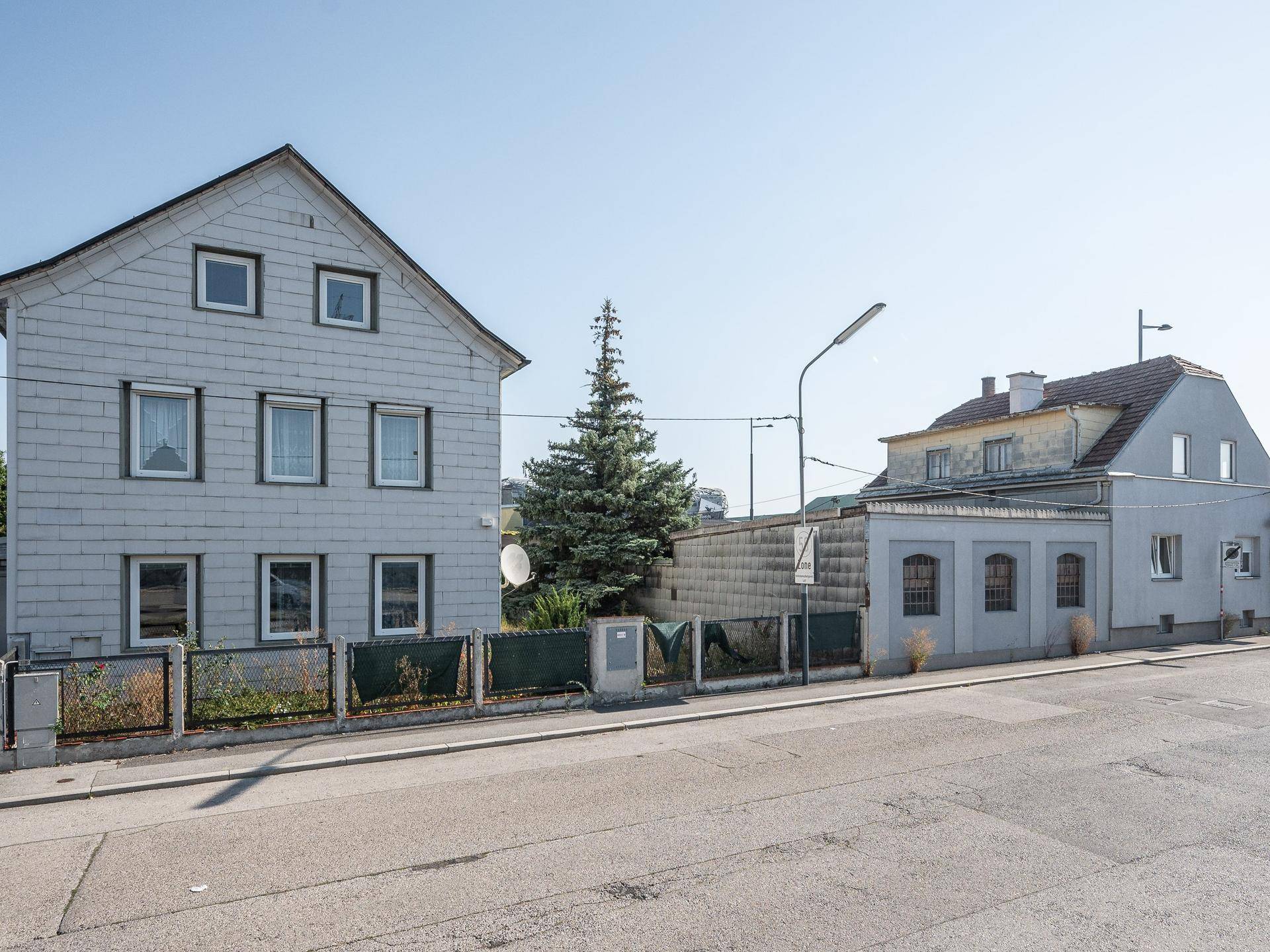 Straßenansicht mit zwei Gebäuden, einem größeren Haus mit Schieferfassade und einem kleineren Nebengebäude.