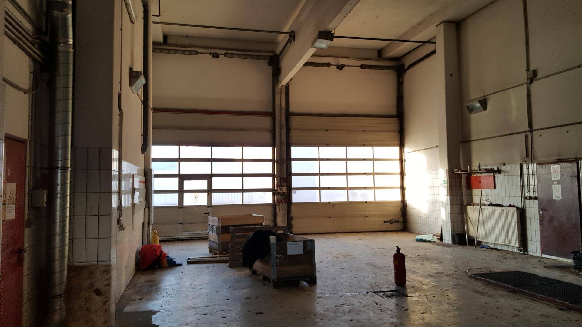 Geräumige Garage oder Lagerhalle mit zwei großen Rolltoren, Fliesenwänden und Betonboden.