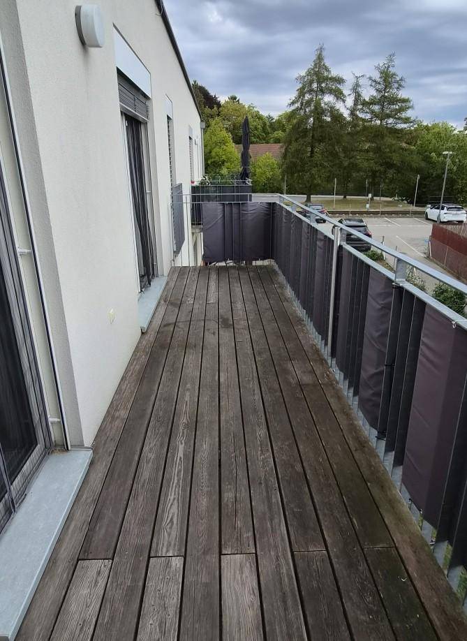 Geräumiger Balkon mit Holzboden und Blick auf die Umgebung unter bewölktem Himmel.
