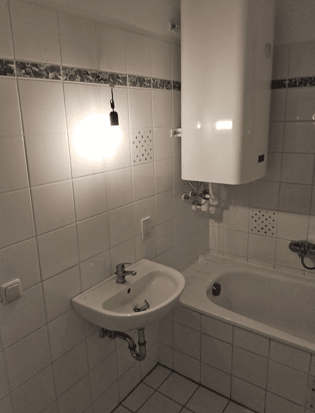 Helles Badezimmer mit weißen Fliesen, Badewanne, Waschbecken und Warmwasserboiler.