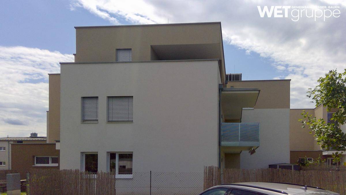 Ansicht eines modernen Wohngebäudes mit klarer Architektur, Balkon und geschlossenen Jalousien an den Fenstern.