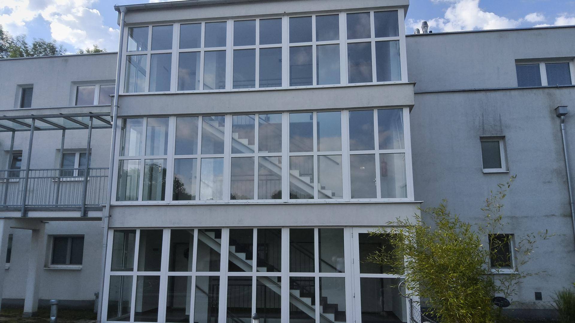 Gebäudeansicht mit einer auffälligen, vollständig verglasten Treppenhauskonstruktion.