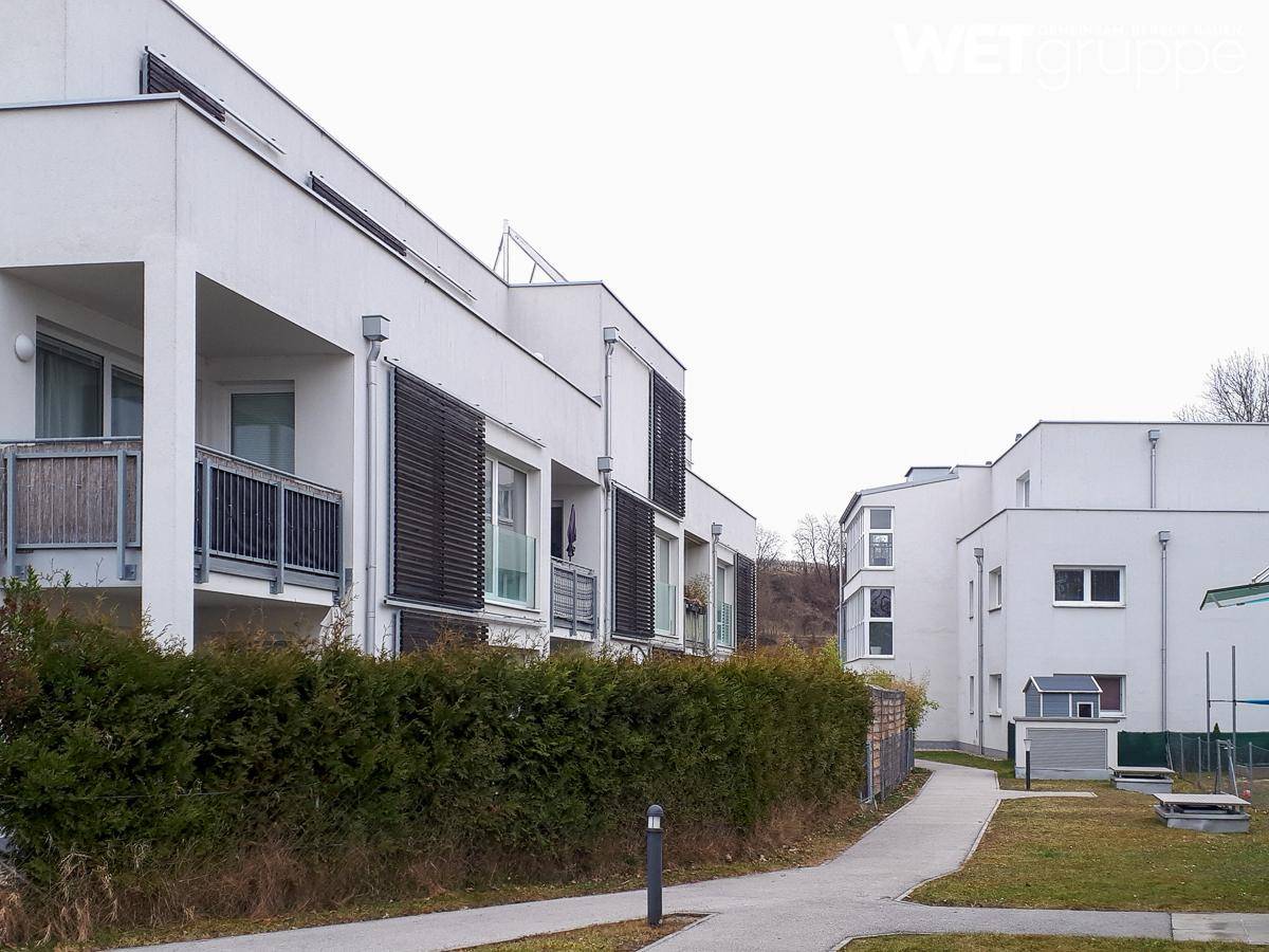 Moderne Wohnanlage mit weißen Fassaden, Balkonen und gepflegten Hecken im Außenbereich.
