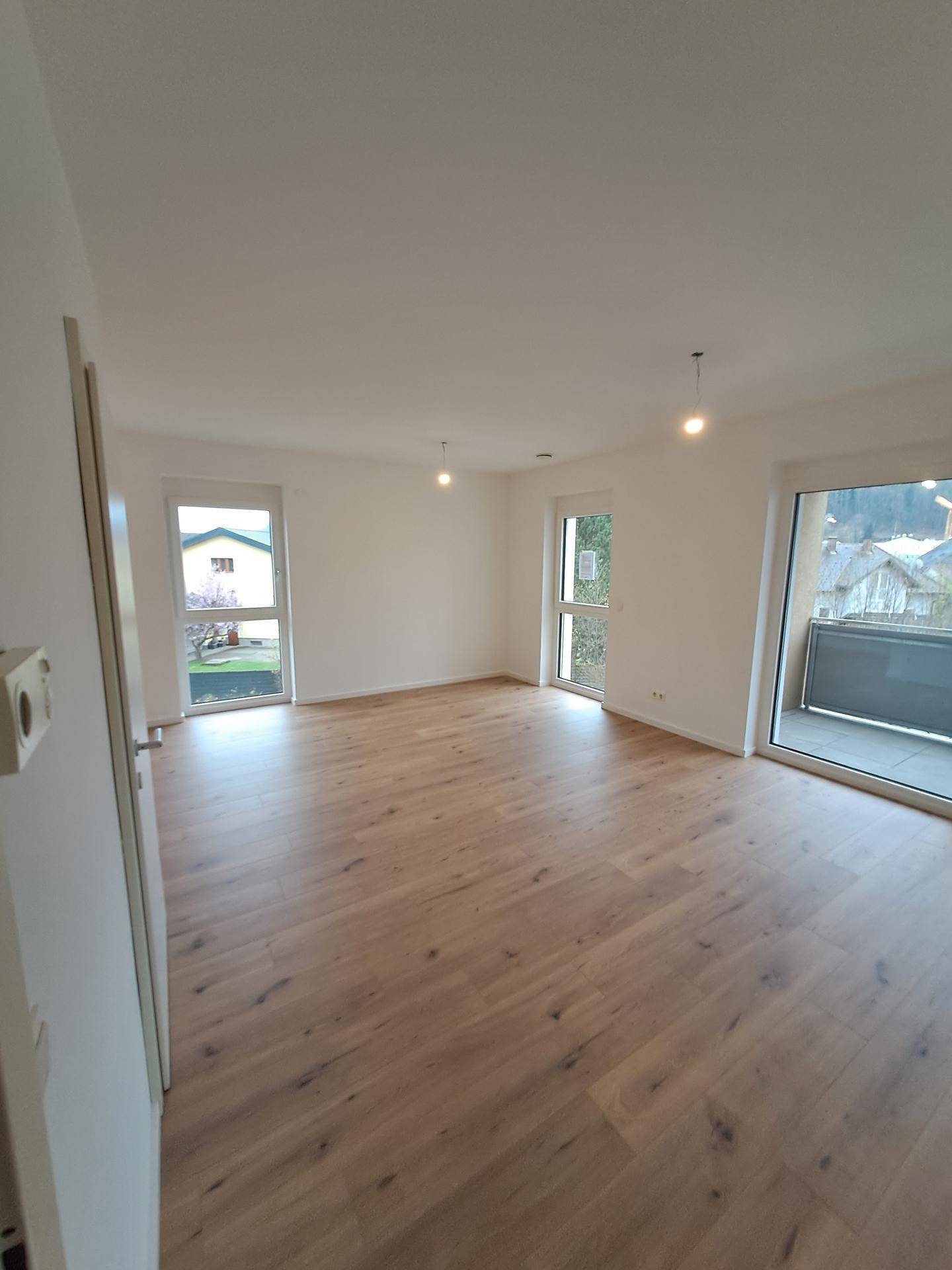 Geräumiges Wohnzimmer mit hellem Holzboden und großen Fenstern für viel Tageslicht.