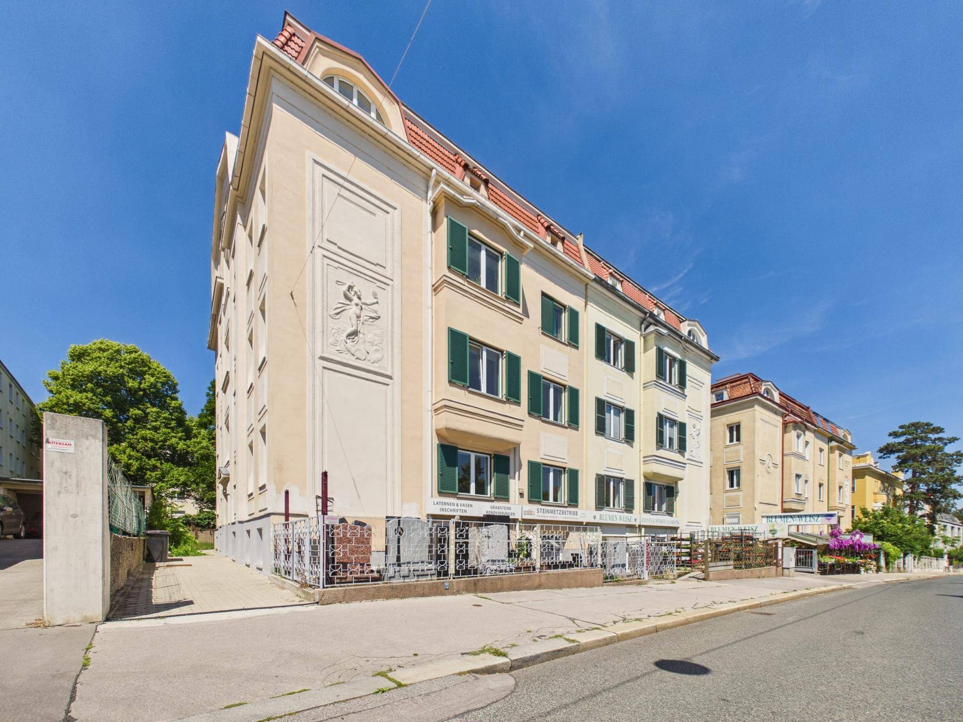Historisches Gebäude mit markanter Fassade, grünen Fensterläden und rotem Dach in städtischer Umgebung.