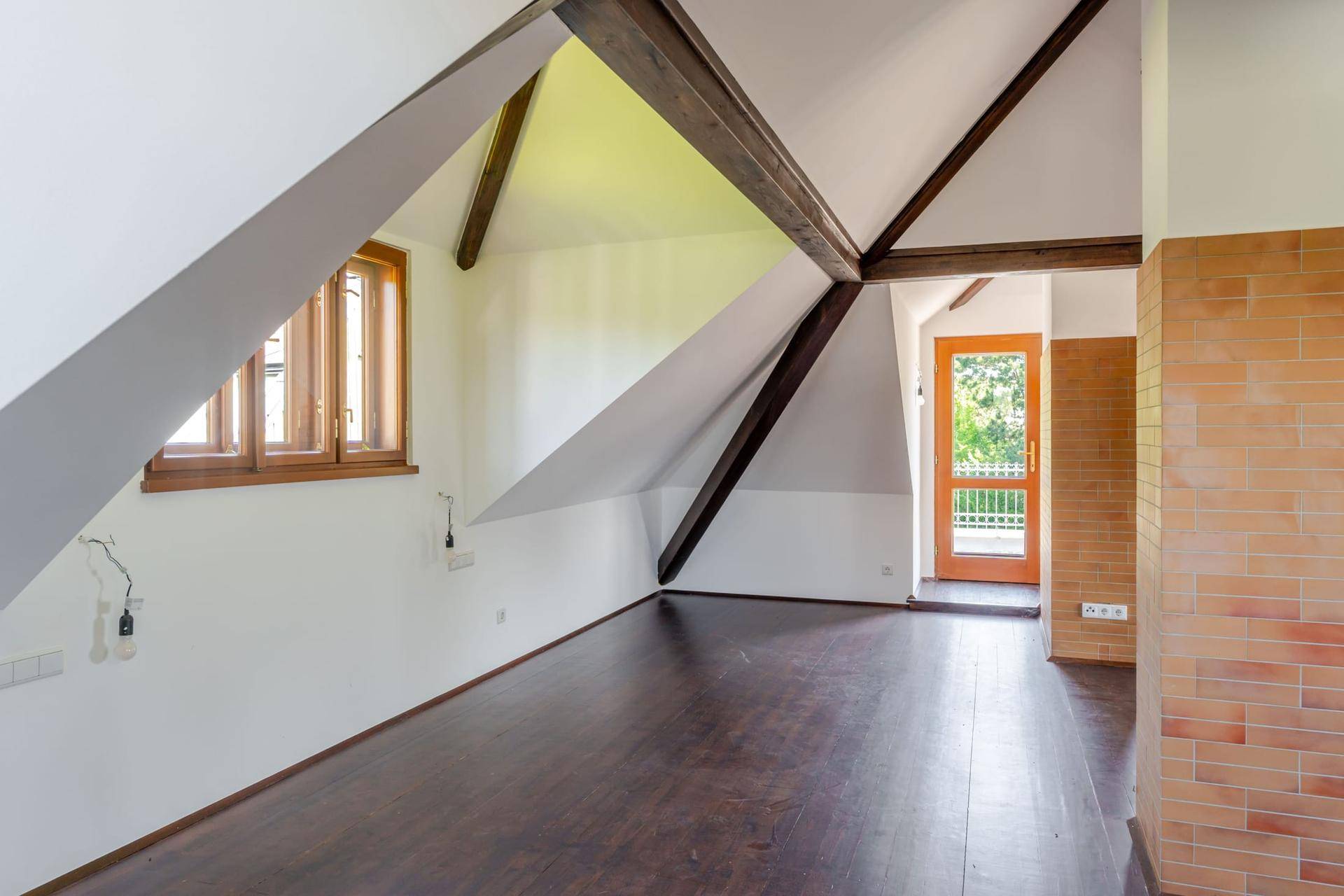Geräumiger Dachbodenraum mit sichtbaren Holzbalken, schrägen Wänden und dunklem Holzboden.