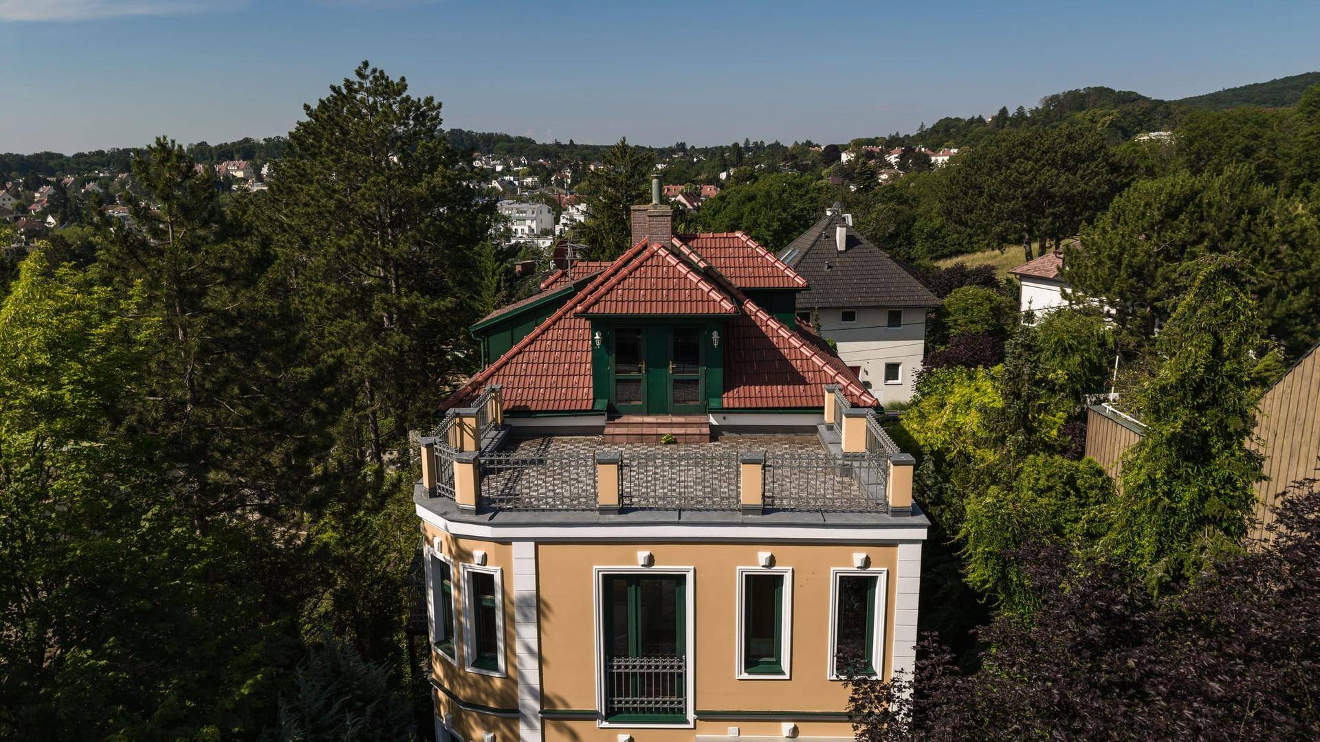Luftaufnahme der Villa mit rotem Ziegeldach und Dachterrasse, umgeben von Bäumen.