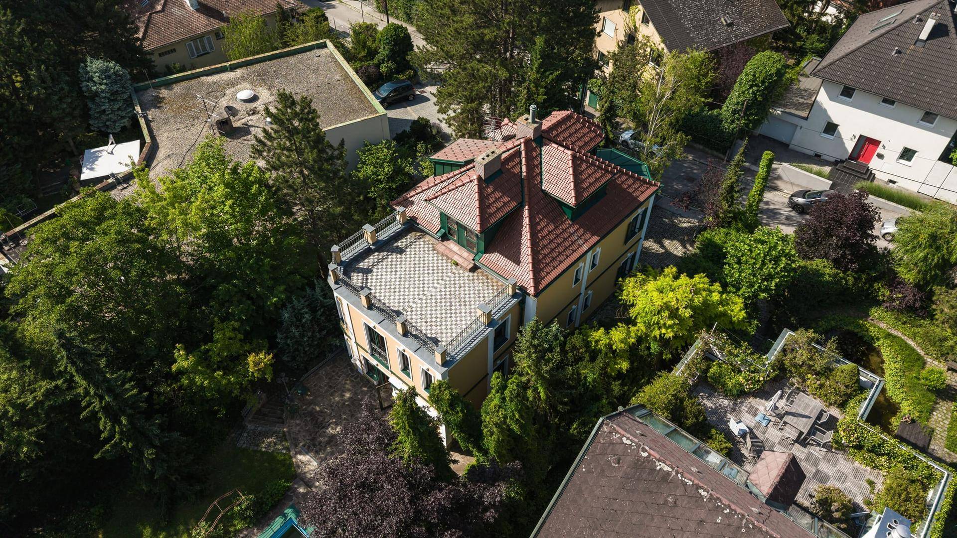 Luftaufnahme der Villa mit rotem Ziegeldach und Dachterrasse, eingebettet in grüne Natur.