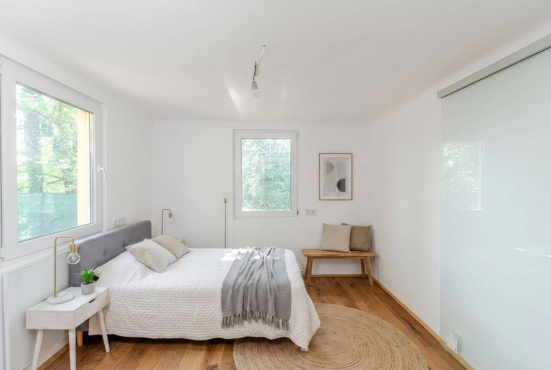Helles Schlafzimmer mit Holzboden, großem Fenster und minimalistischer Einrichtung.