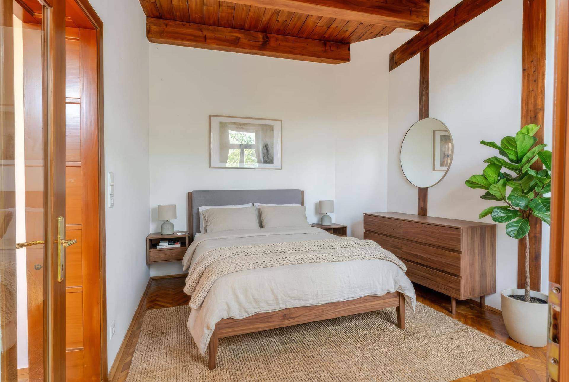 Gemütliches Schlafzimmer mit Holzbalkendecke, Holzboden und modernem Bett.