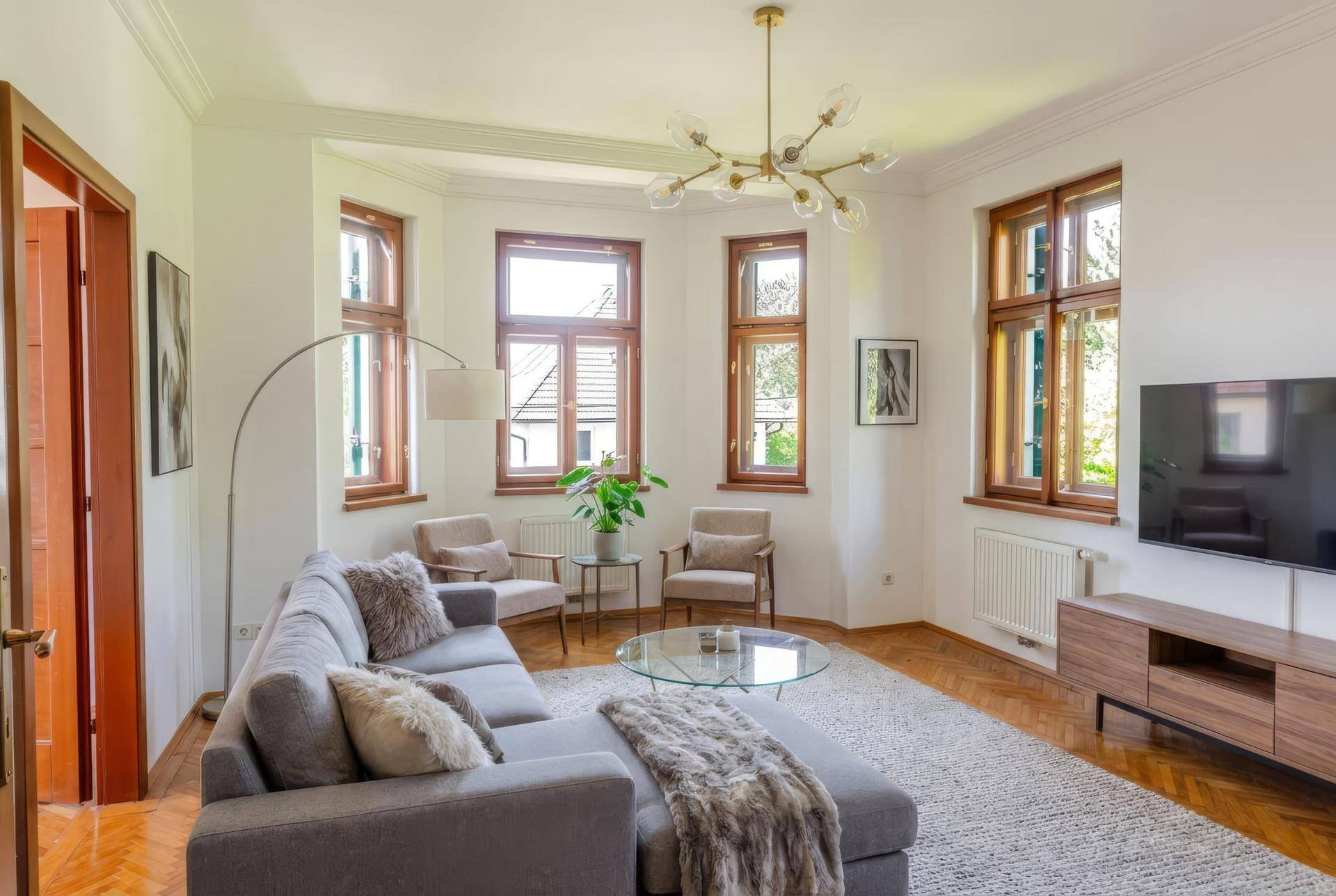 Helles Wohnzimmer mit Parkettboden, großen Fenstern und bequemer Couch, modern eingerichtet.