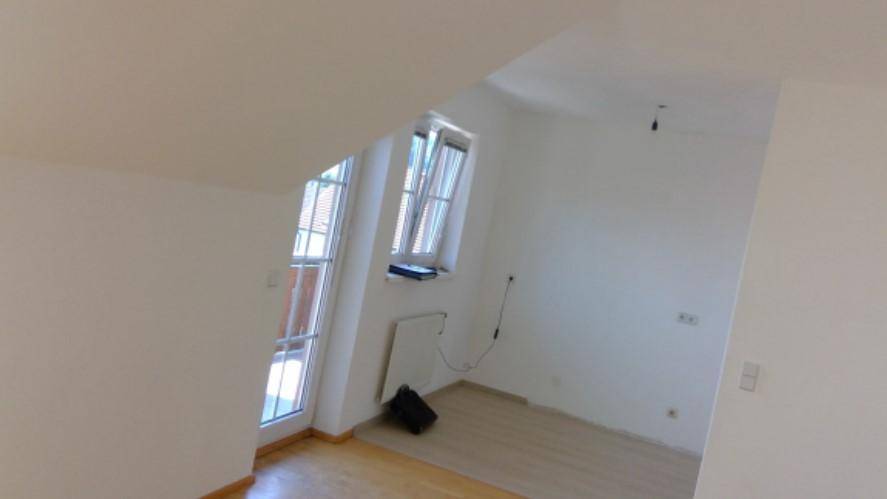 Heller Raum im Dachgeschoss mit schrägen Wänden und Zugang zu einem Balkon.