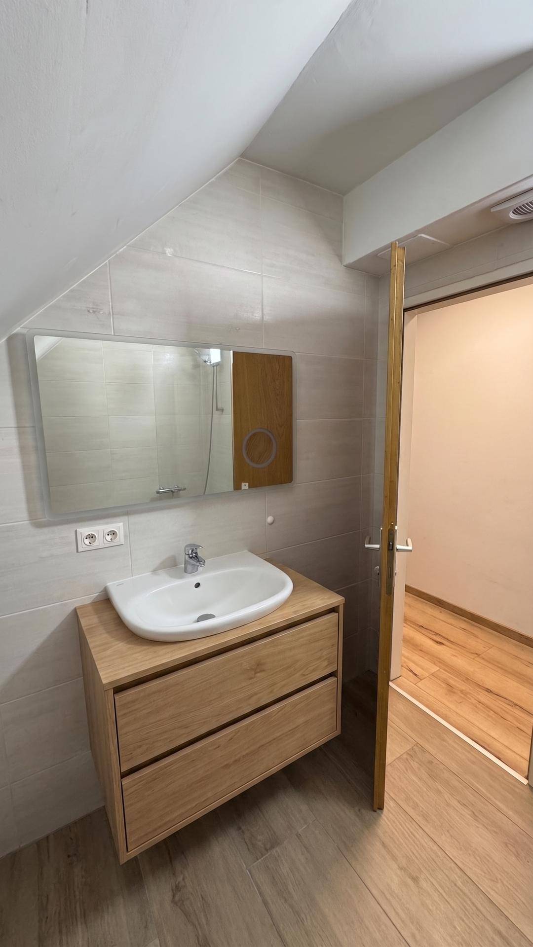 Badezimmer mit modernem Waschtisch, Spiegel und beigefarbenen Wandfliesen.