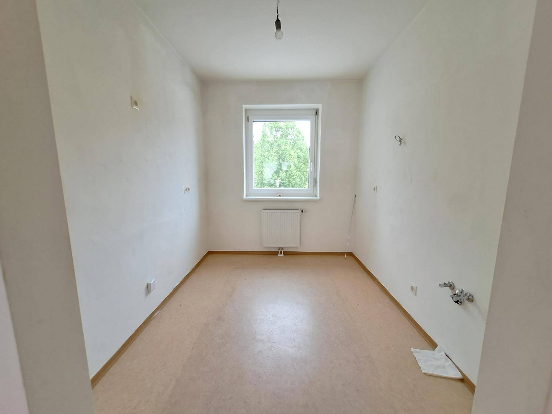 Leeres Zimmer mit Linoleumboden, Fenster und Heizkörper.