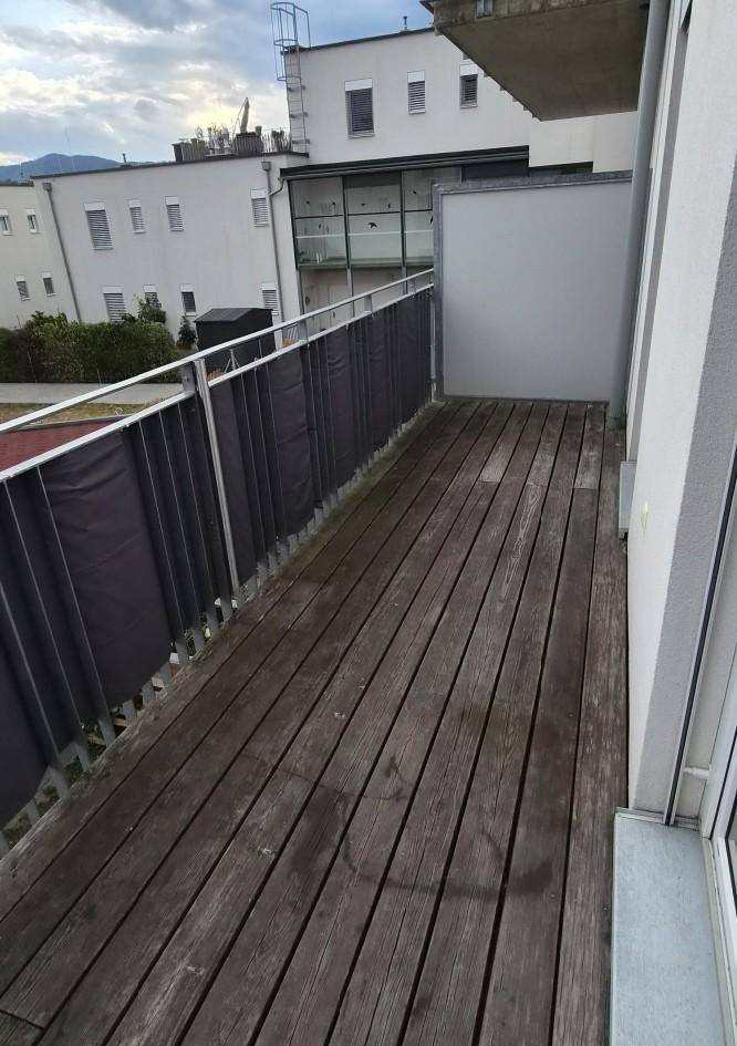 Langer Balkon mit Holzdielen und Metallgeländer, bietet Platz für Entspannung im Freien.