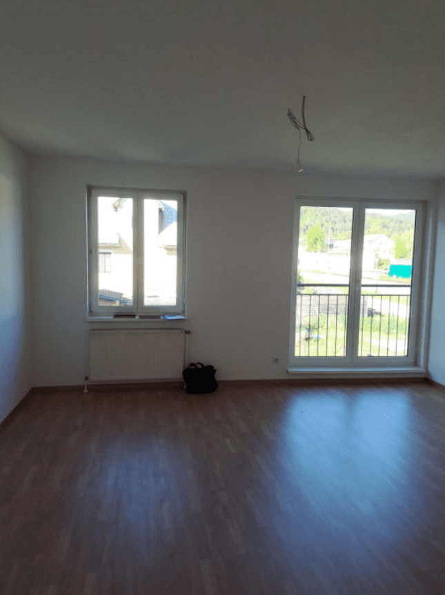 Heller Wohnraum mit Laminatboden, Heizkörper und Zugang zu einem französischen Balkon.
